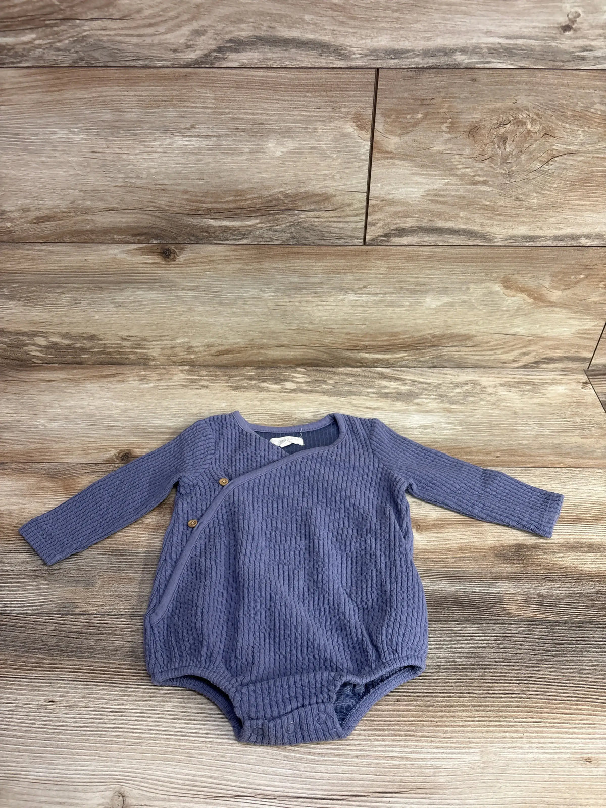 Flat lay of purple ribbed kimono bubble romper showing long sleeves, diagonal snap closure and snap crotch on wood floor
