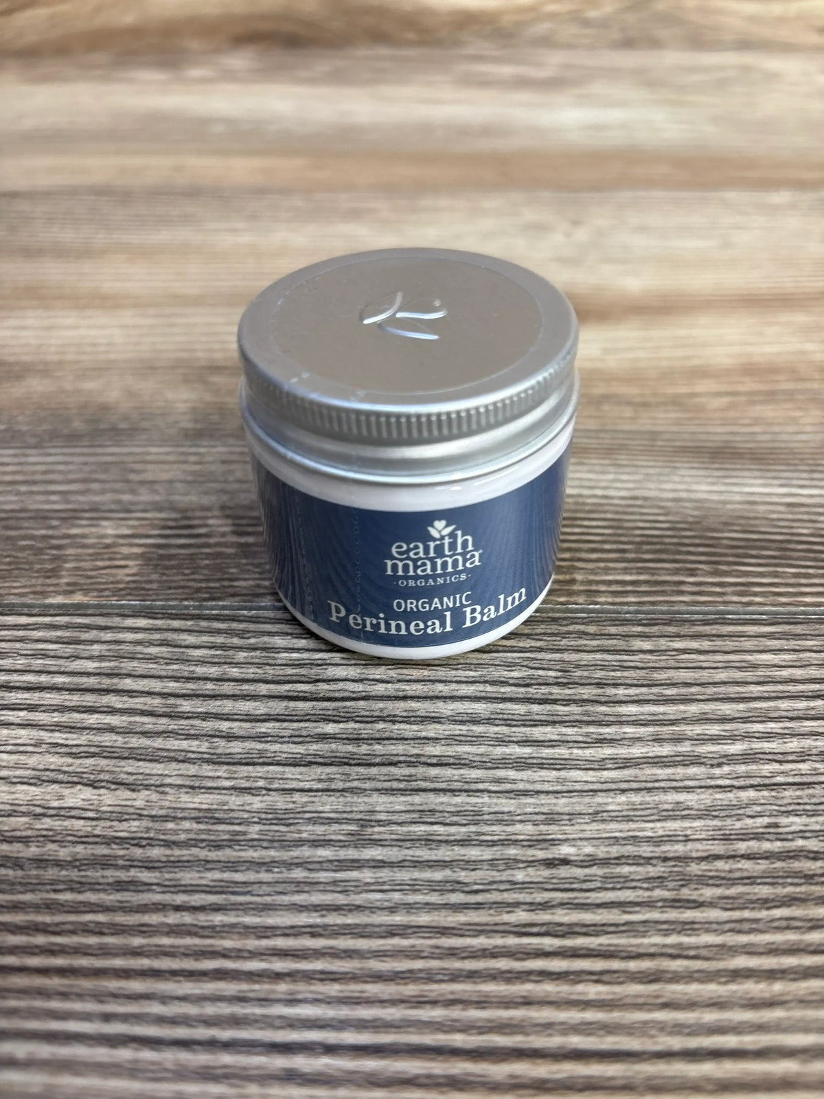 Front view of NEW Earth Mama Organic Perineal Balm 2oz showcasing its labeled jar on a wood-grain surface
