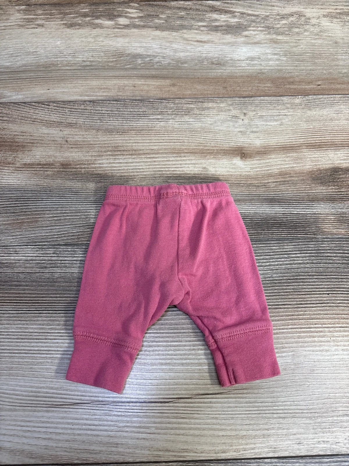 Front view of Simple Joys pink preemie pants in size Preemie showcasing ribbed ankle cuffs on a wood grain background