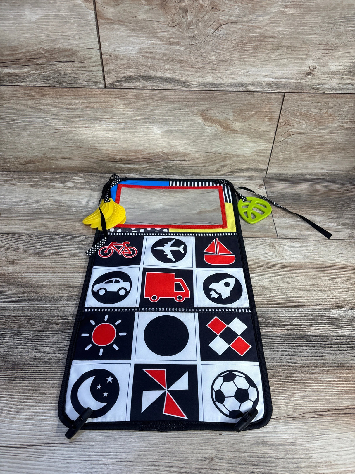 Top-down view of Alibaba tummy time cloth book with high-contrast icons, mirror with red trim, and yellow and green teethers