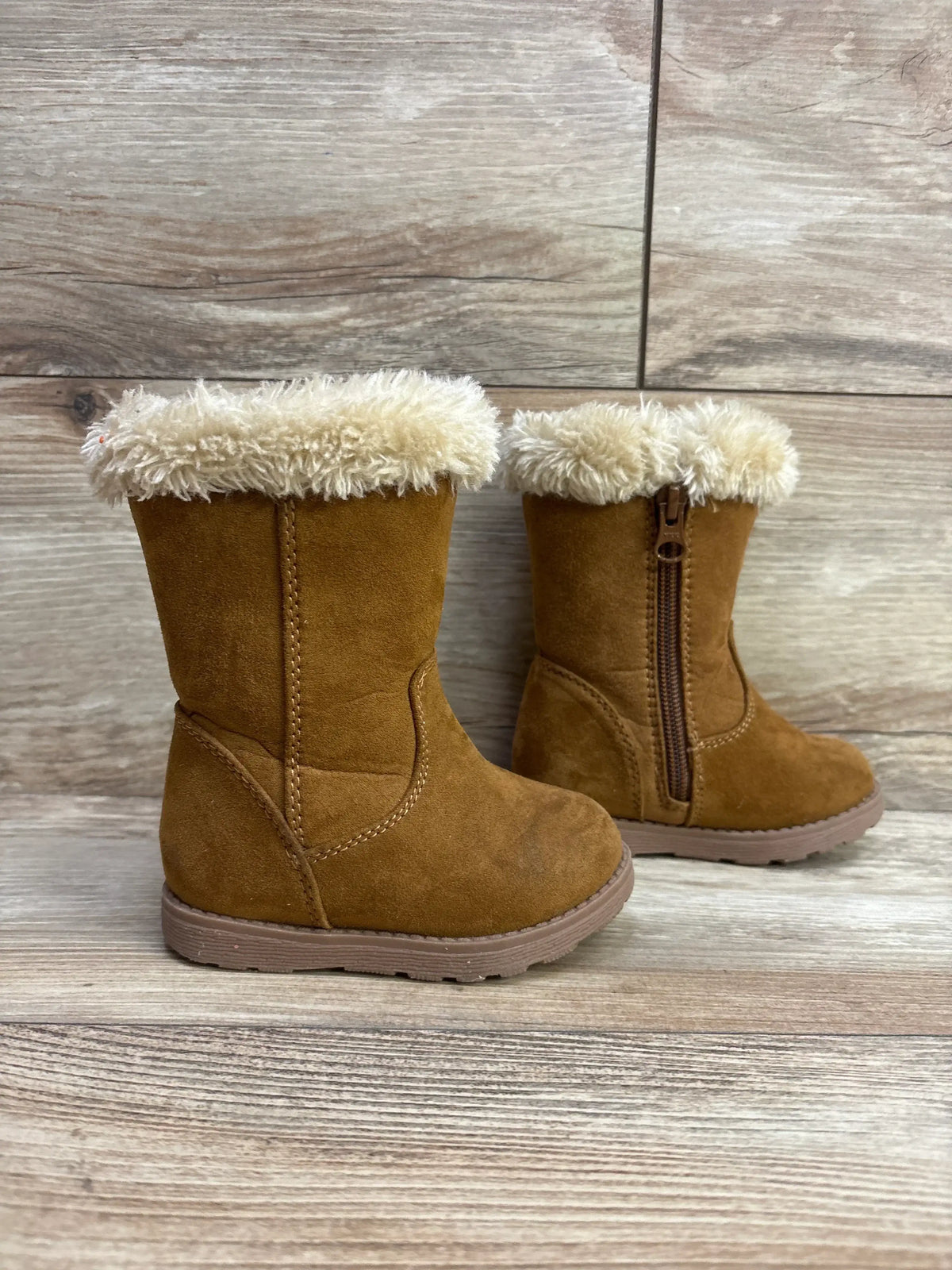 Pair of brown toddler boots with fuzzy cream lining and side zipper on wood floor