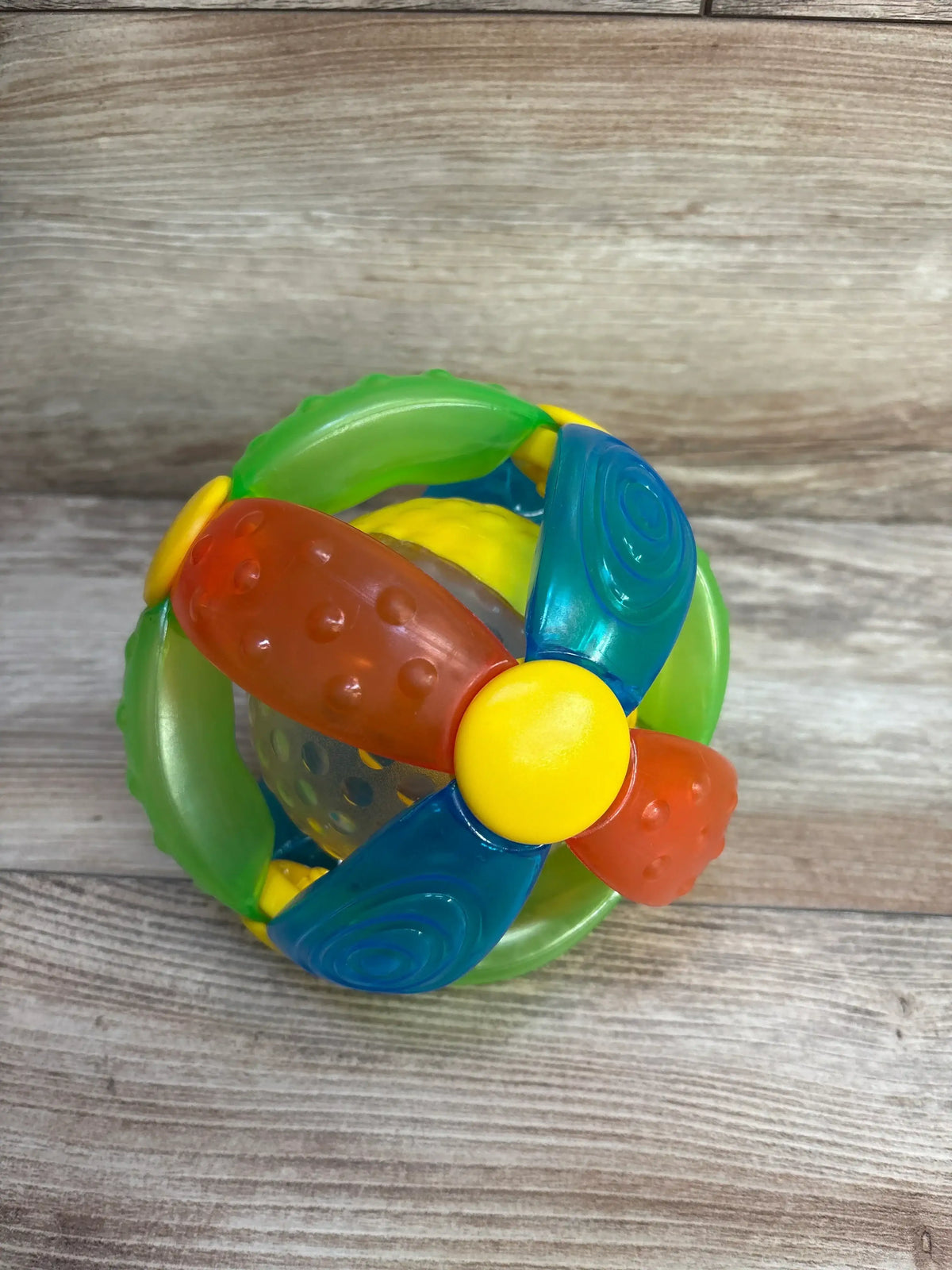Top view of B Kids Blink’n Bling Ball showcasing multicolor textured grips and inner clear rattle ball on light wood background