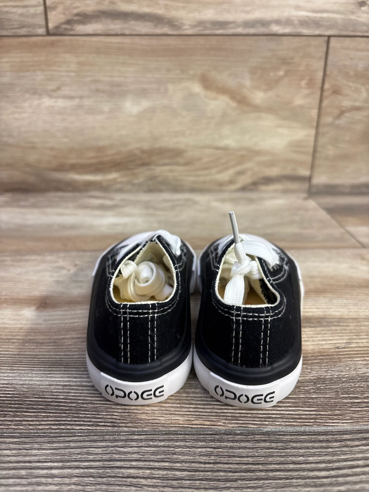 Rear view of OPOEE low-top black sneakers showing tied white laces and OPOEE heel logo on wood floor