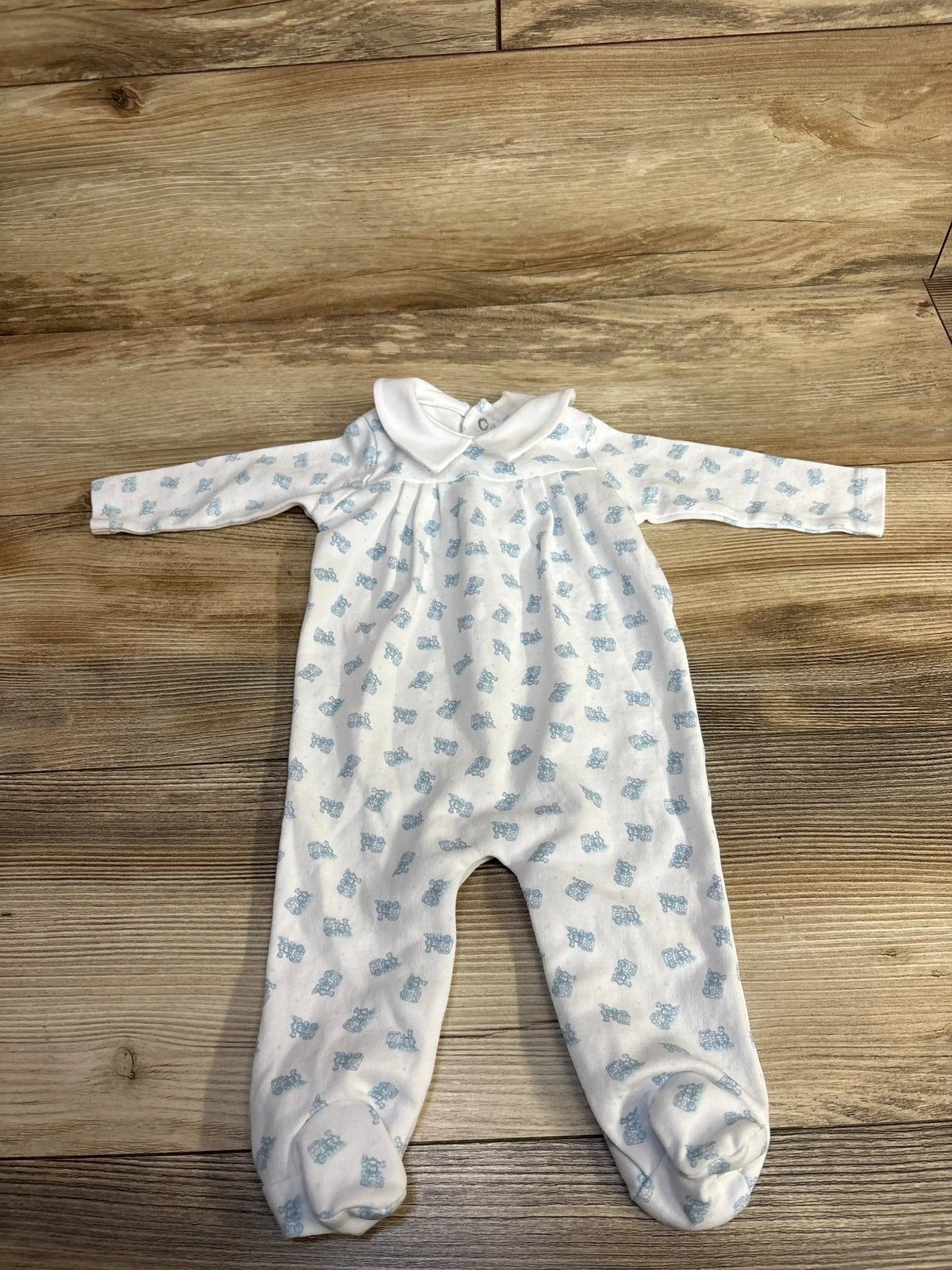 Flat lay of white Edgehill Train Footie showcasing blue train print, long sleeves, footed legs, and collar on wood floor