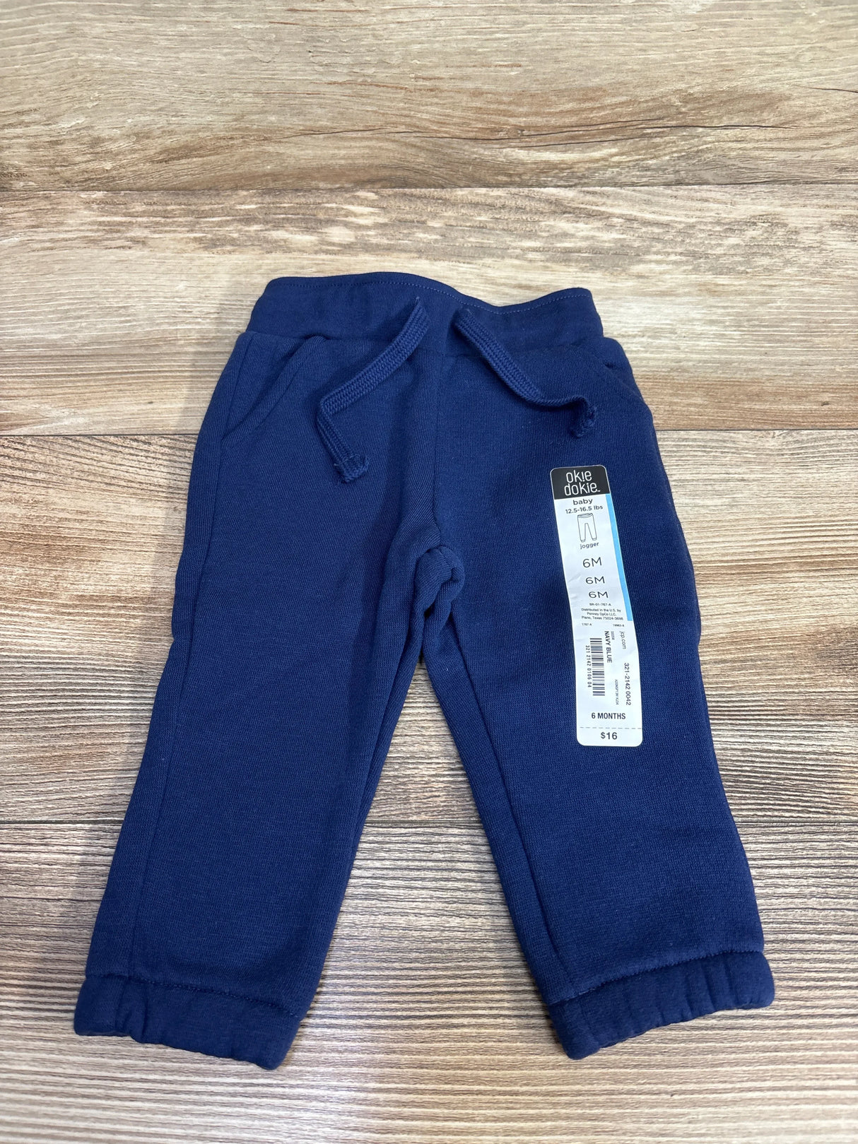 Navy blue baby jogger pants with drawstring and elastic cuffs on wooden surface, size 6 months