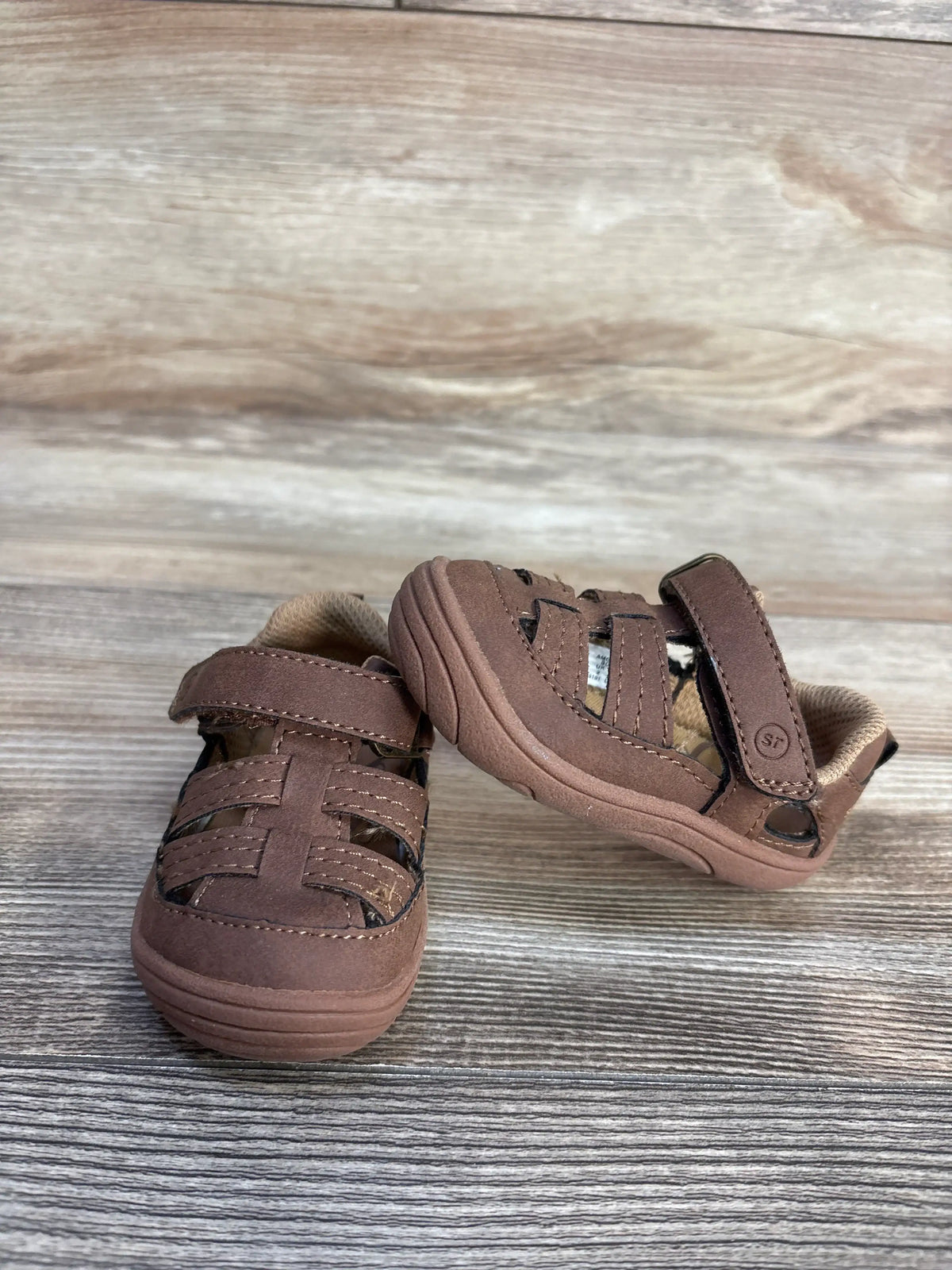 Brown Stride Rite Amos 3.0 fisherman sandals for toddlers on a wooden surface