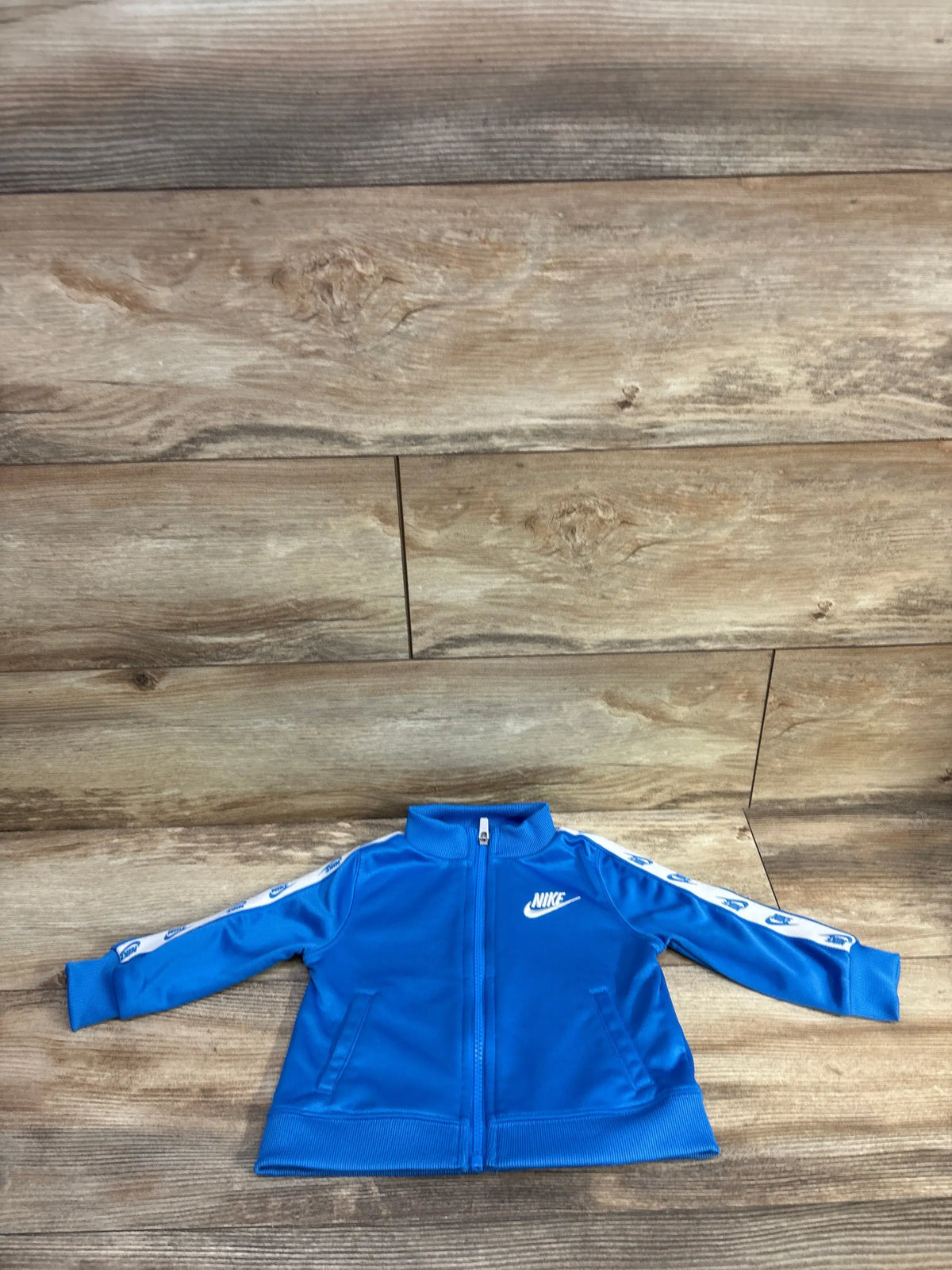 Front view of Nike full zip taped track jacket showcasing blue color and taped sleeves on a wood-patterned background