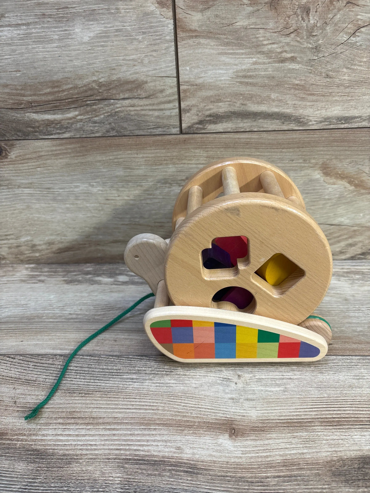 Front view of Bajo wooden snail sortroller showcasing colorful shape-sorting holes and pull cord on a wood floor
