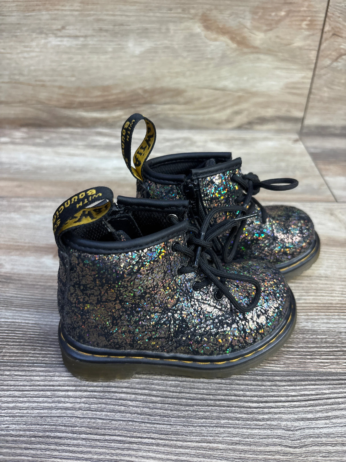 Three quarter view of toddler Dr Martens 1460 metallic boots showing iridescent finish and yellow stitched sole on wood