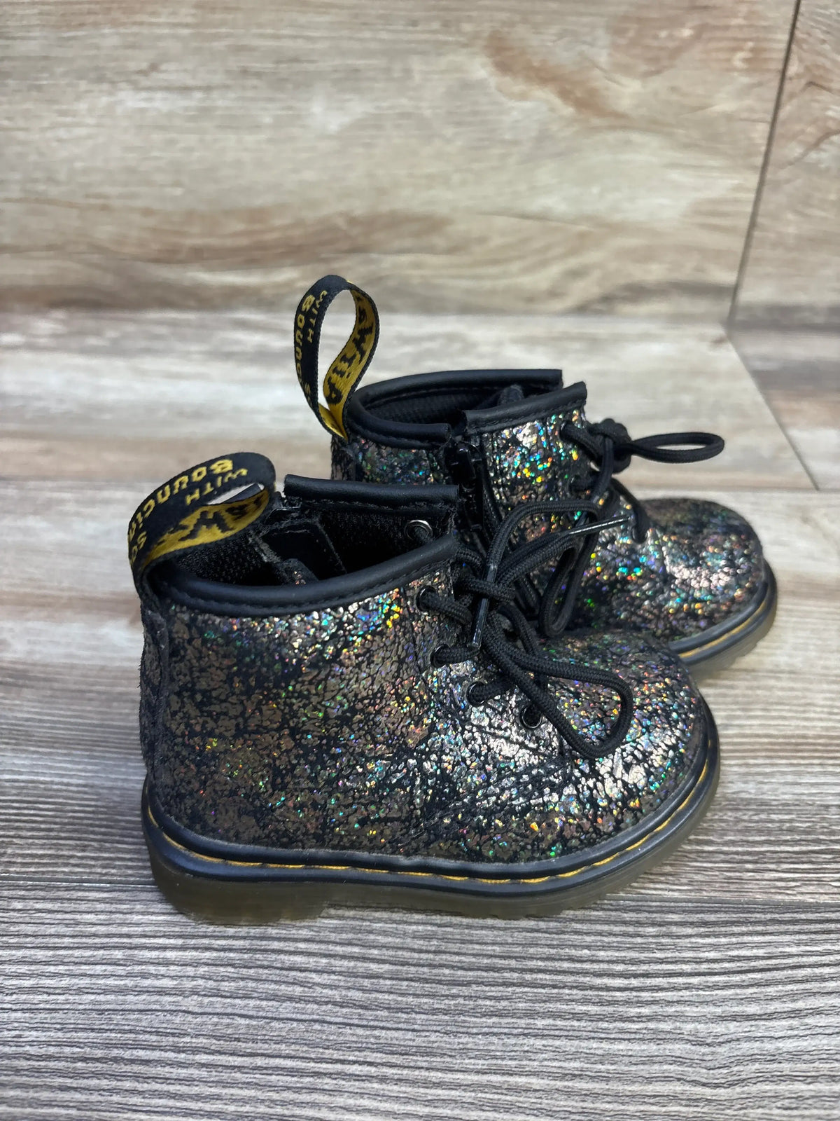 Three quarter view of toddler Dr Martens 1460 metallic boots showing iridescent finish and yellow stitched sole on wood