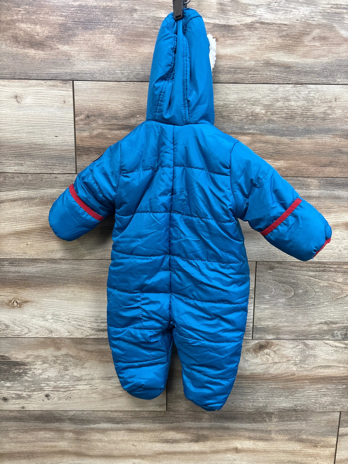 Back view of a blue Ben Sherman baby snowsuit with red sleeve accents hanging on a wood wall.