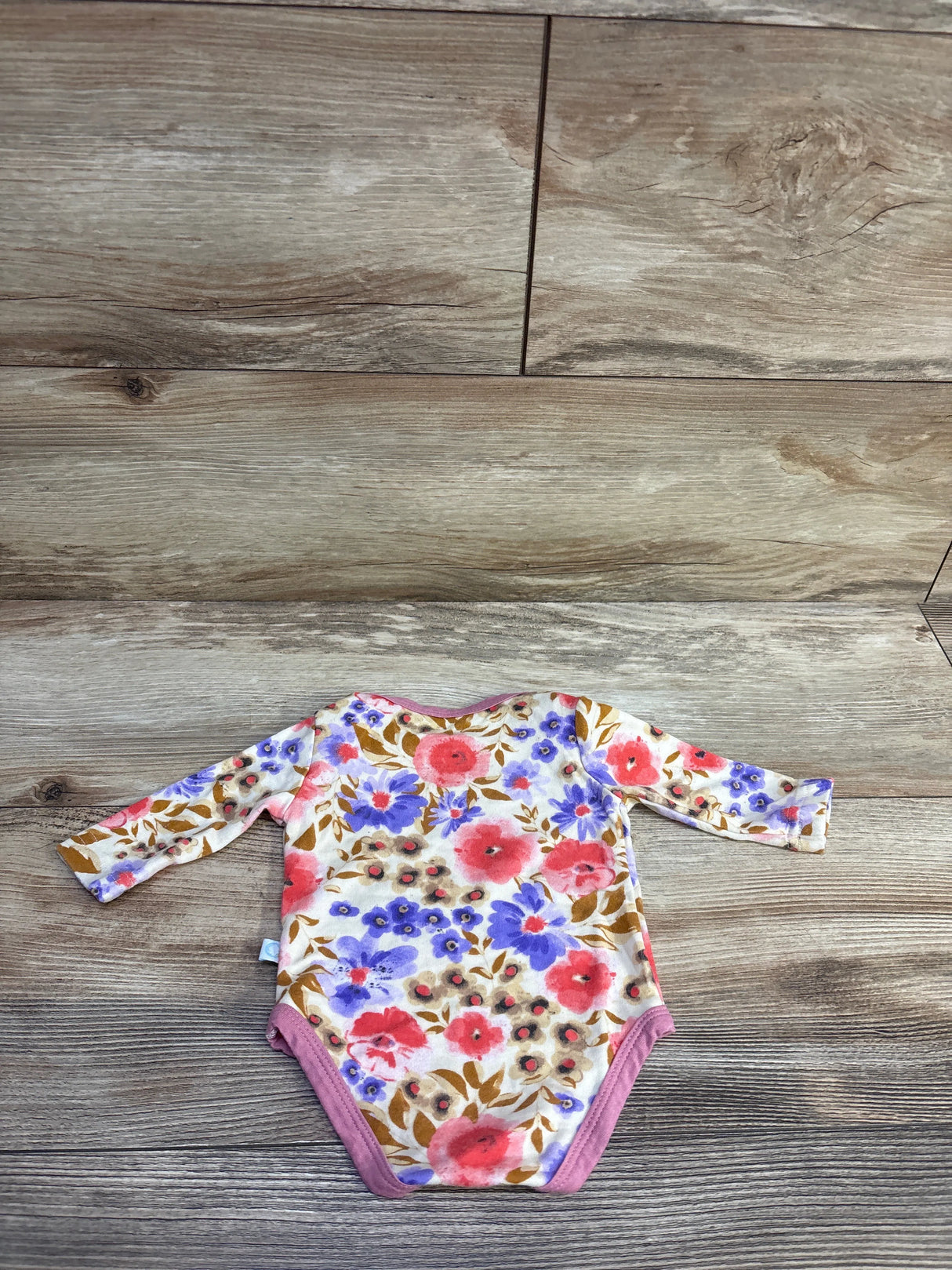 Flat lay of Dreamland Baby bamboo floral long-sleeve bodysuit in cream showing pink trim and floral print on wood background