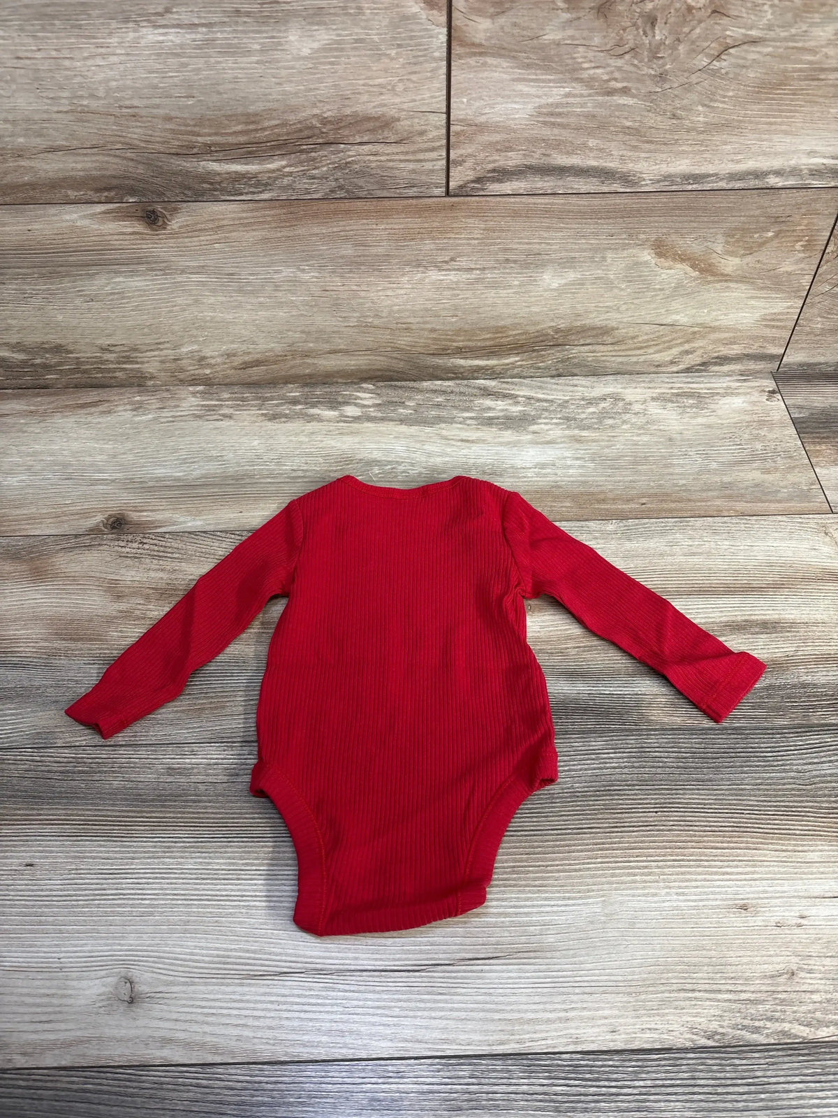 Red ribbed long sleeve baby bodysuit on wood floor background