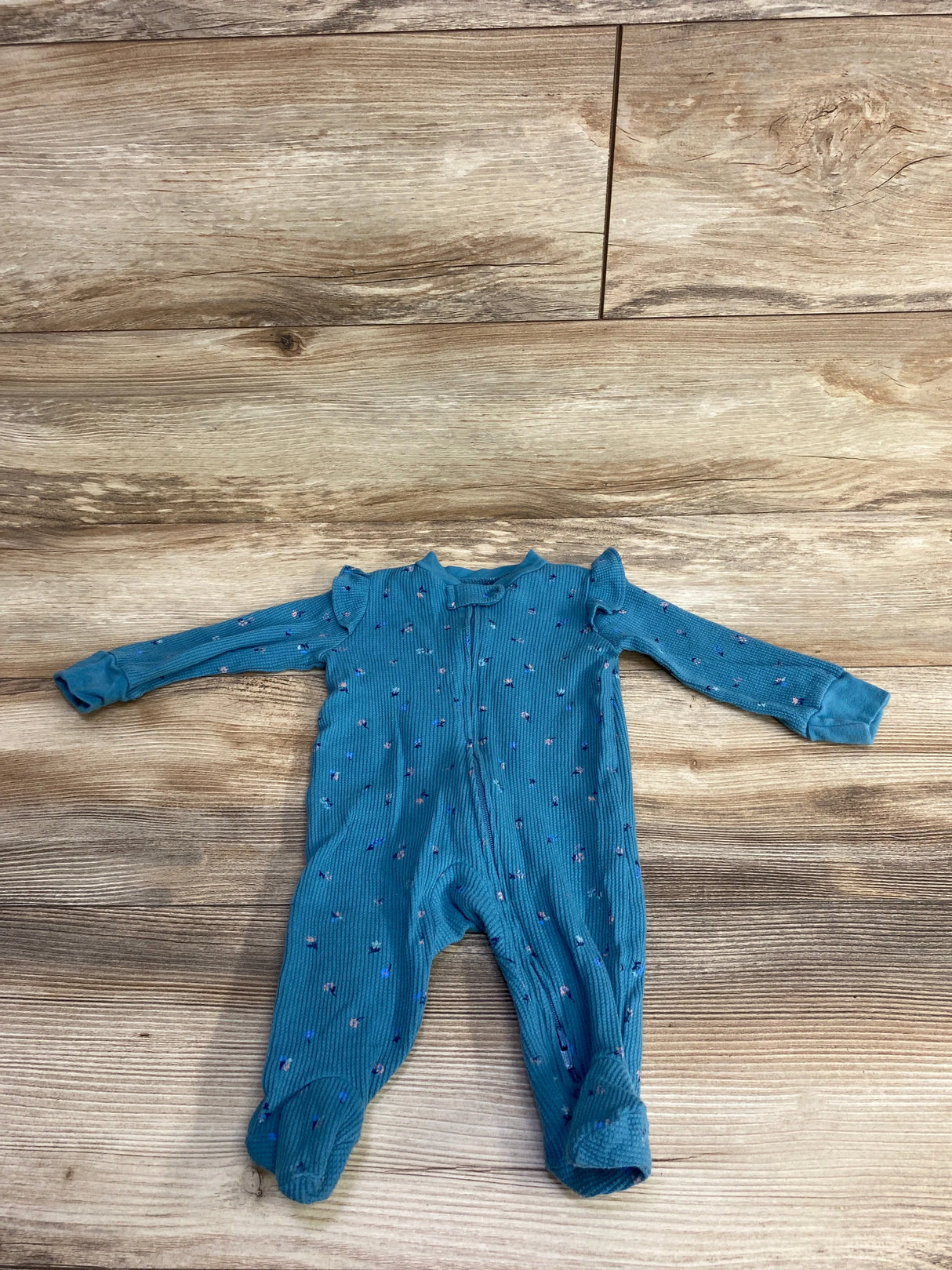 Blue long-sleeve baby onesie with small pink and blue floral print on wood floor