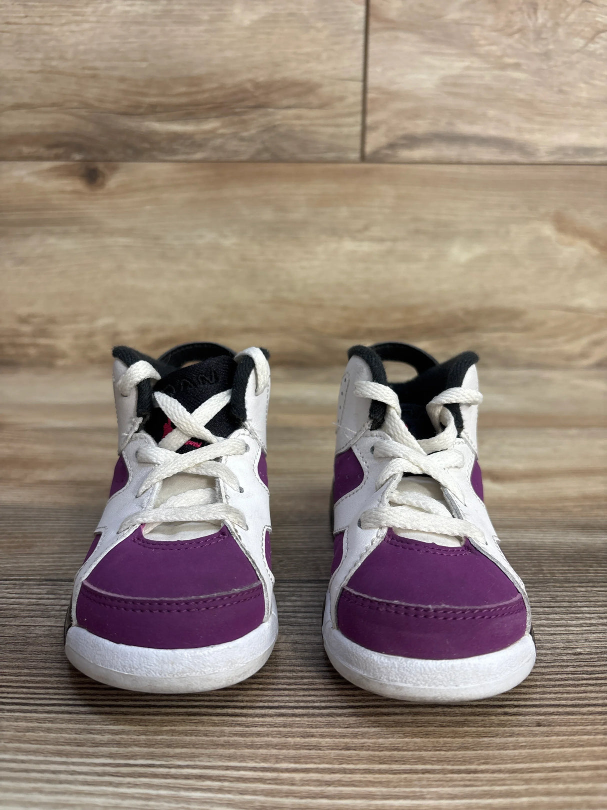 Purple and white toddler sneakers with laces on wooden floor background