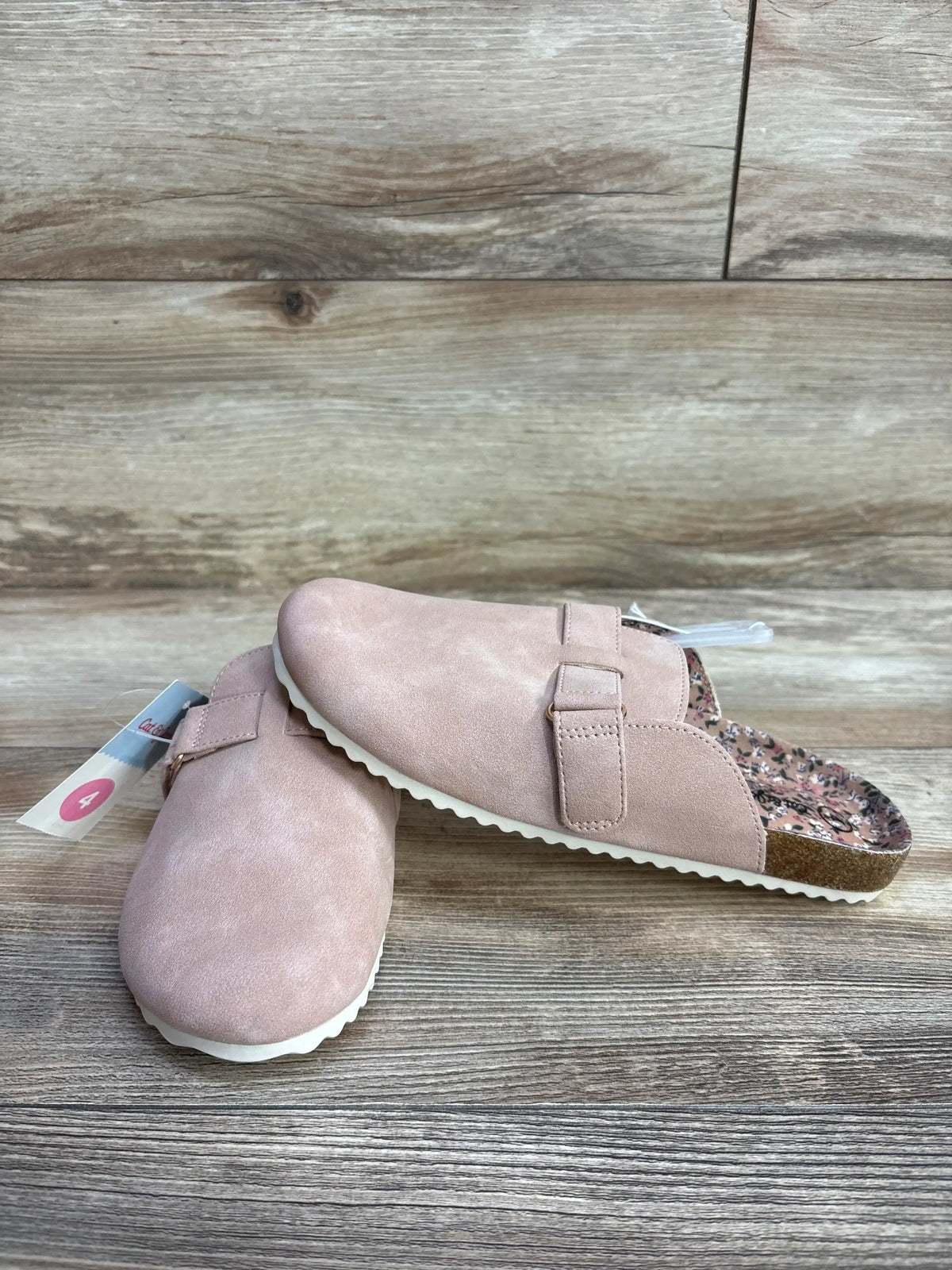 Pink suede slip-on clogs for kids with buckle detail on wood background