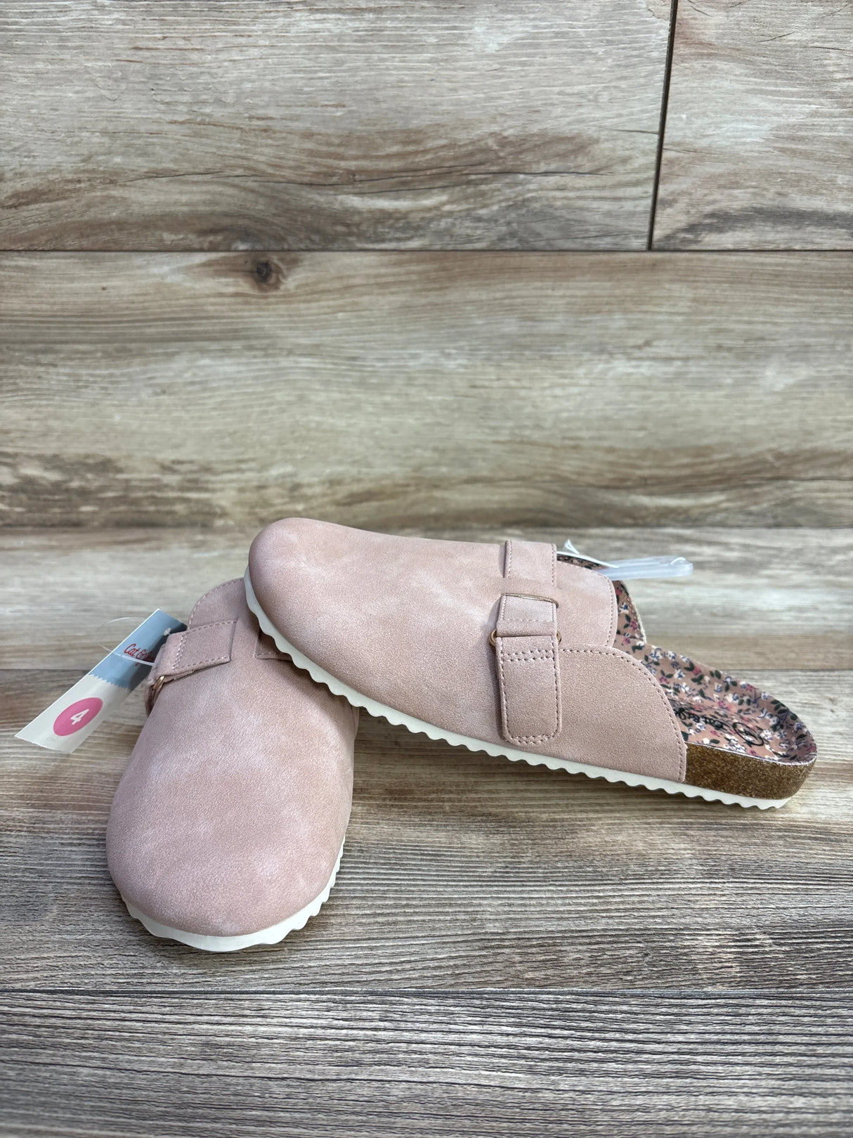 Pink suede slip-on clogs for kids with buckle detail on wood background