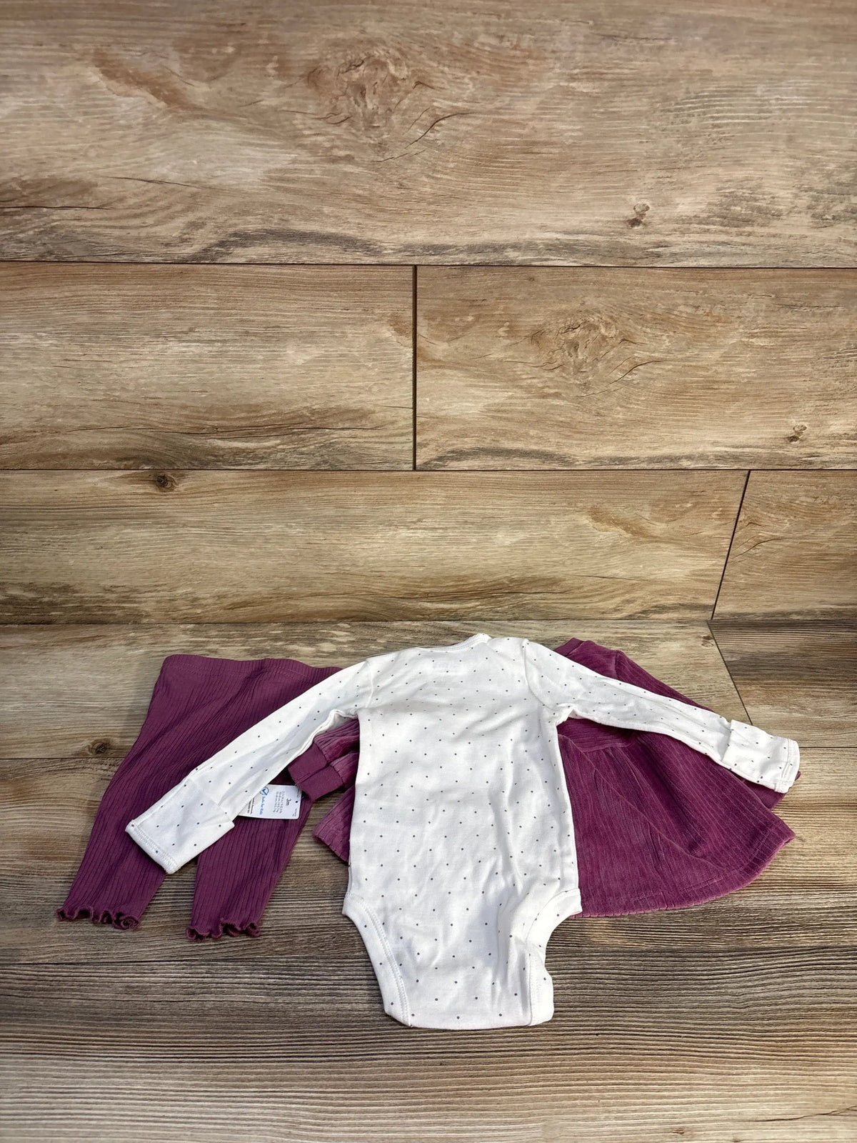 Flat lay of mauve three-piece baby outfit with white dotted snap bodysuit, velvet ruffle top, and ribbed leggings