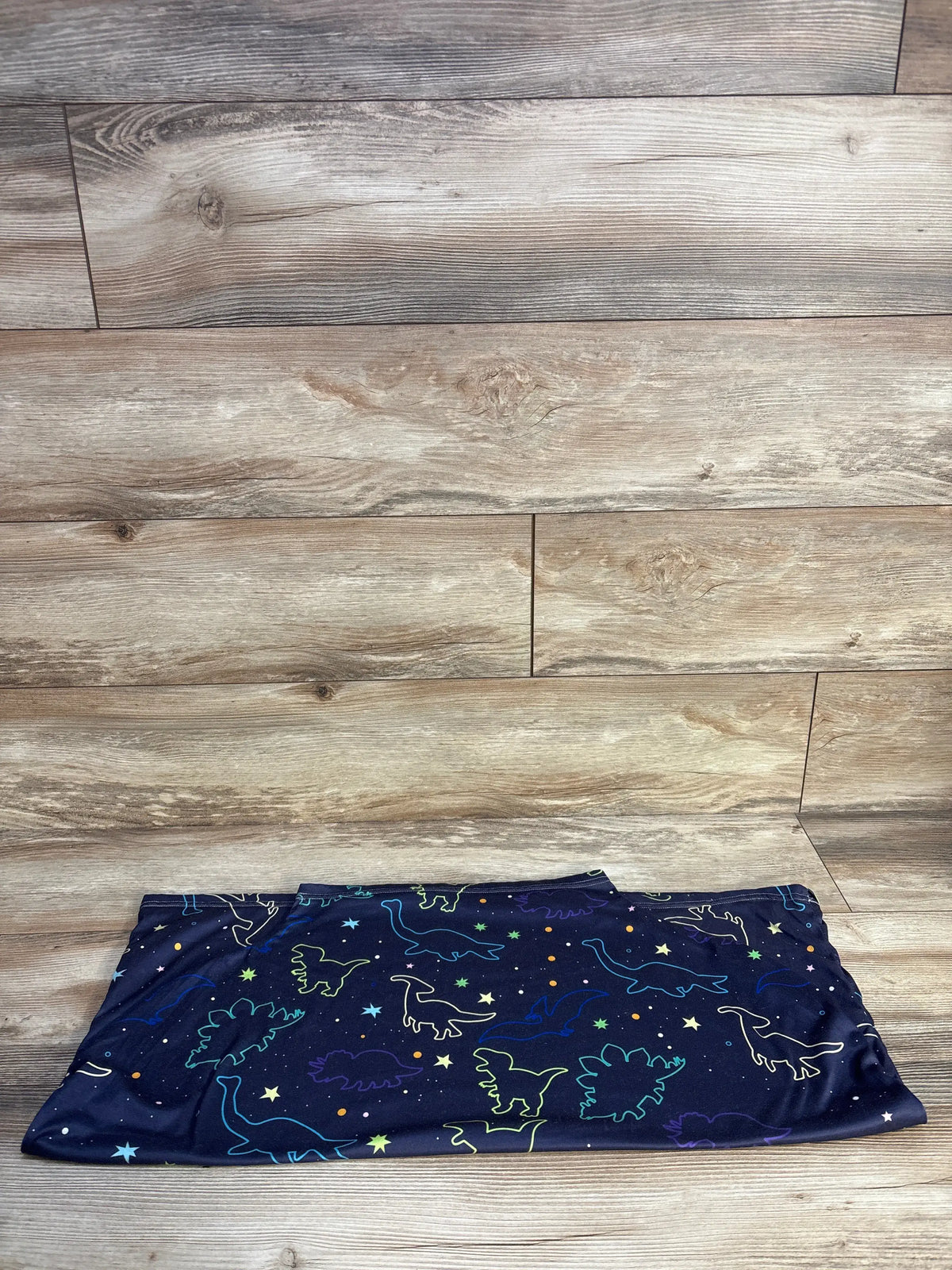 Top view of dinosaur print multi-use nursing and car seat cover showcasing navy dinosaur pattern on a wood floor