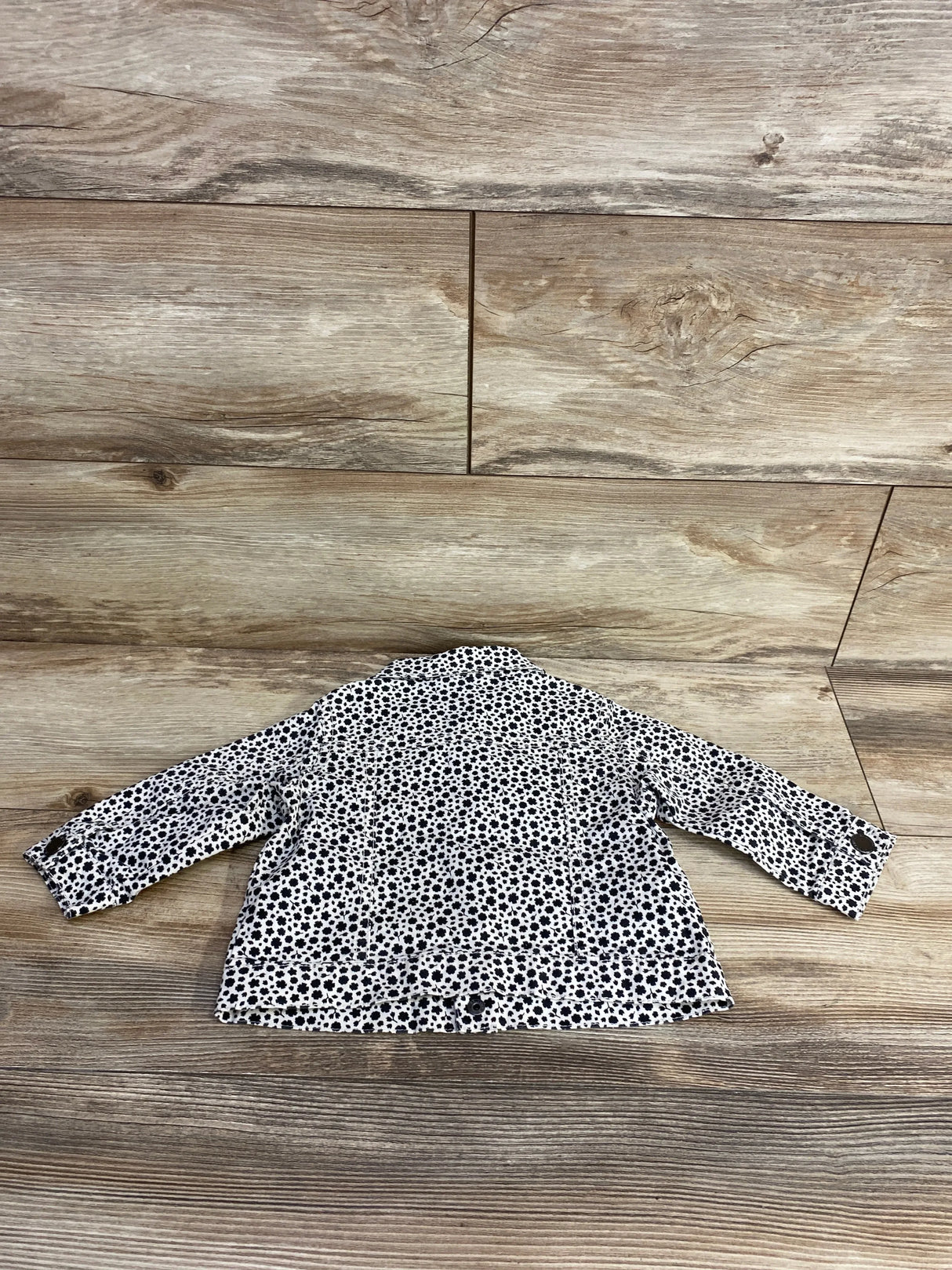 Back view of a toddler's white jacket with black flower print on wooden floor background