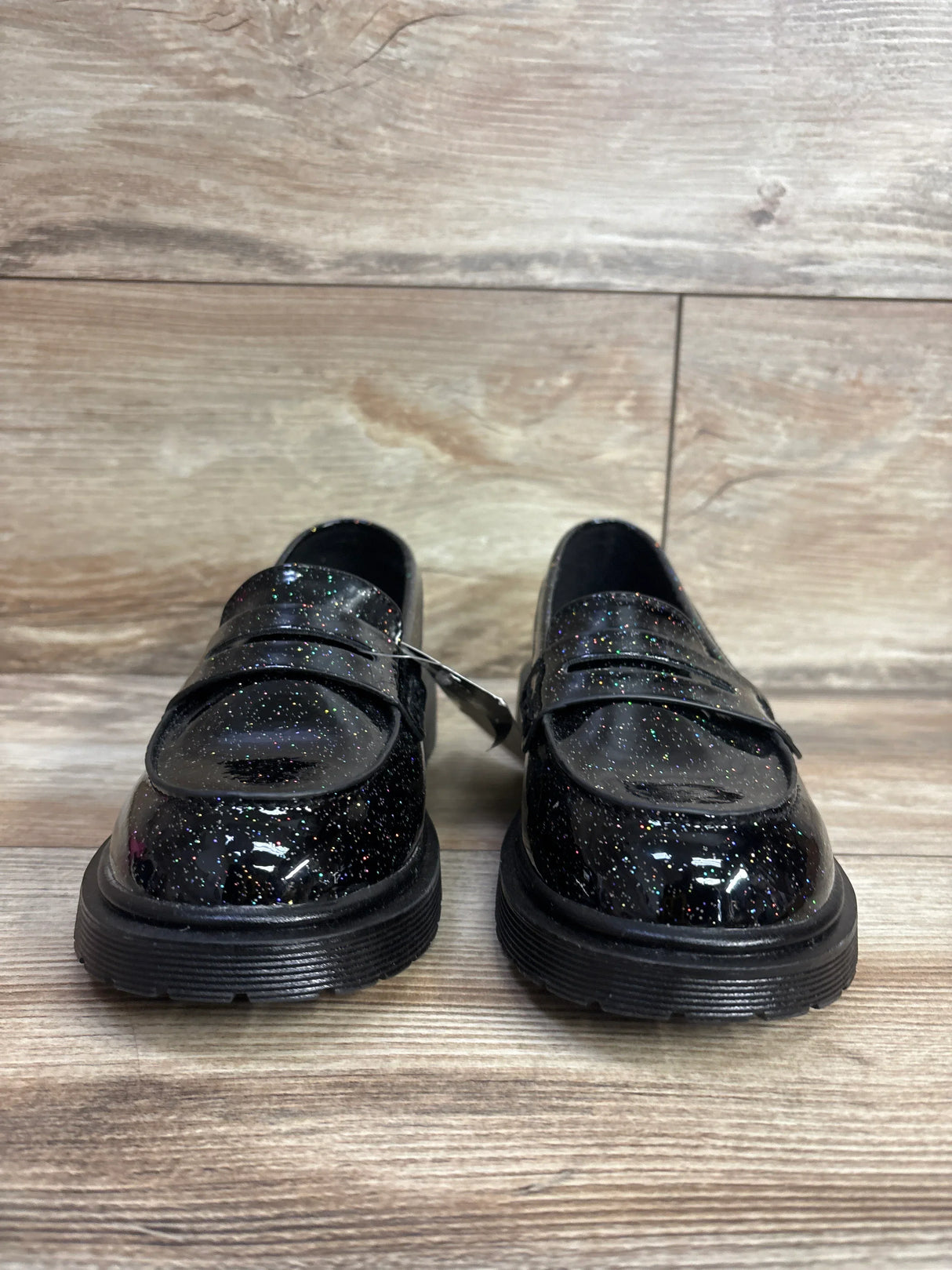 Children's black glitter dress shoes on wood floor, shiny patent loafer style