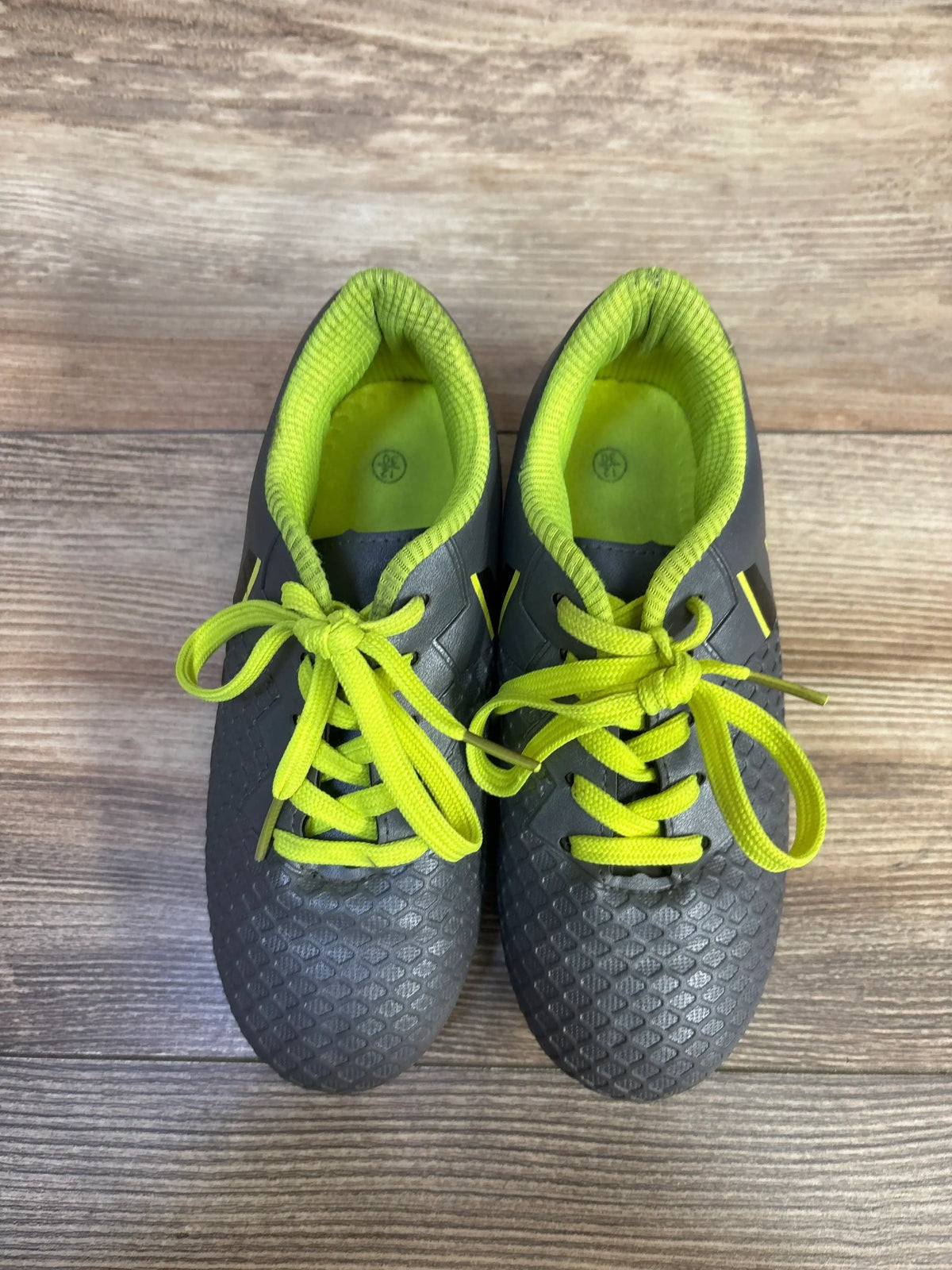 Overhead view of Hawkwell soccer cleats size 12C, grey with neon yellow laces and lining, textured upper on wood floor