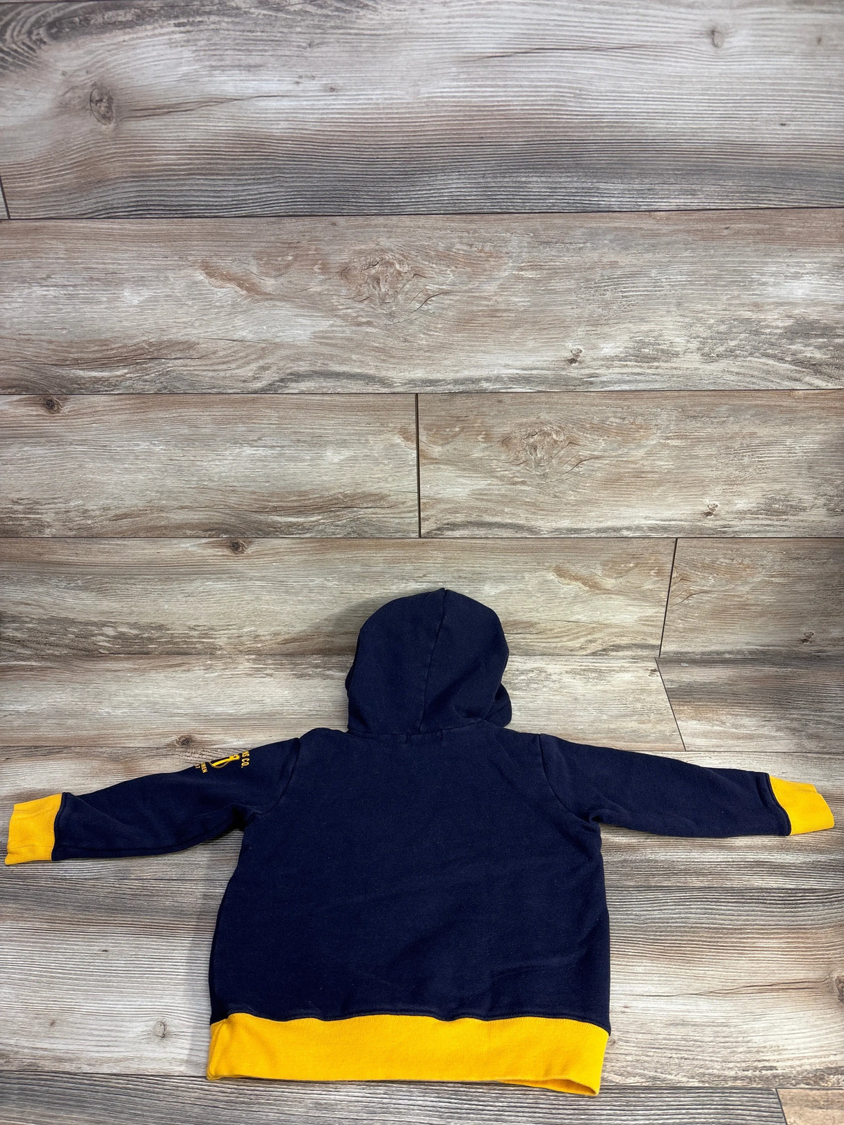 Navy blue toddler hoodie with yellow cuffs and hem, laid flat on wood surface.