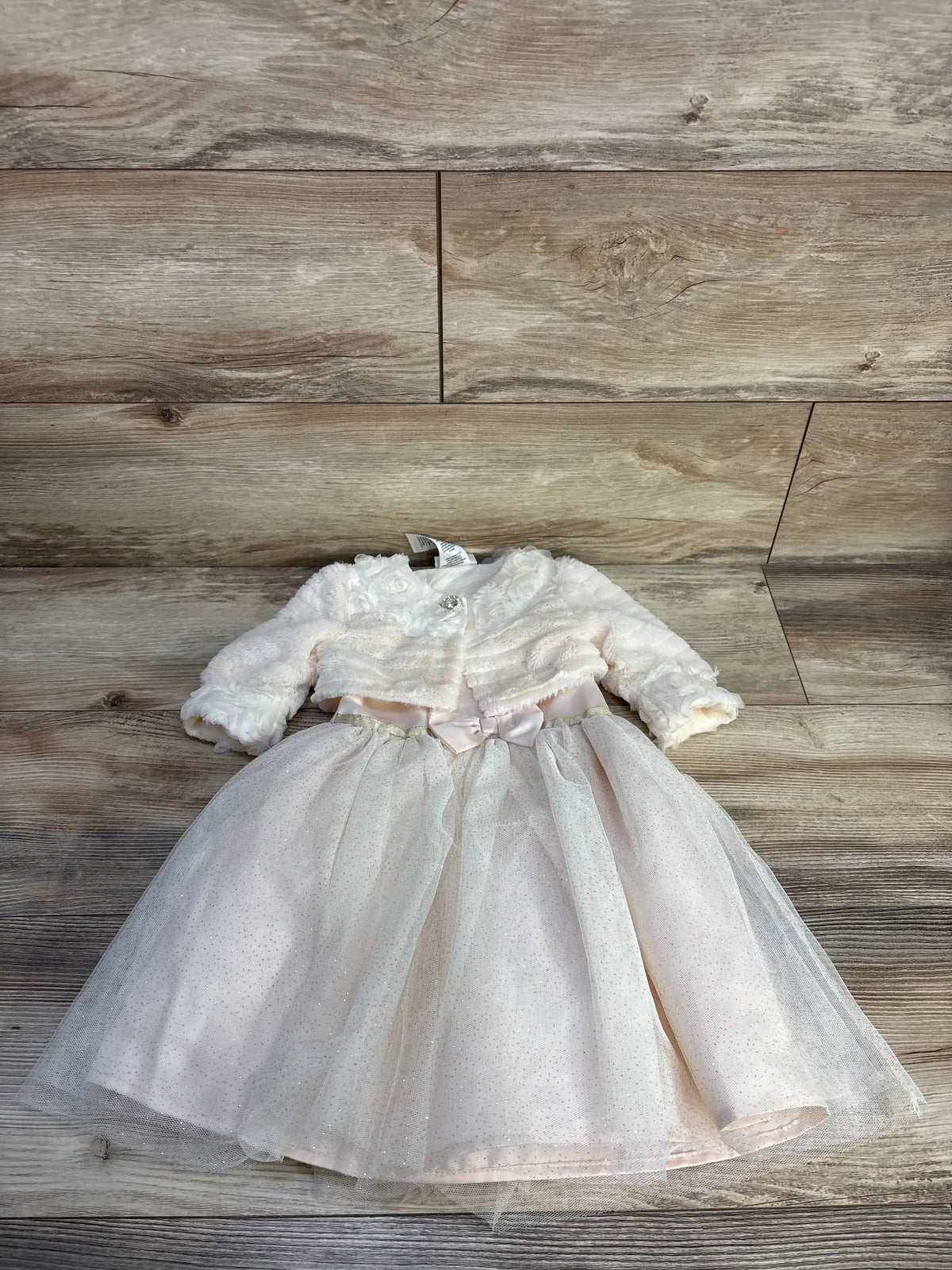 Top-down of ivory toddler ballerina dress with glitter tulle skirt and satin bow, plus faux-fur cardigan on wood floor
