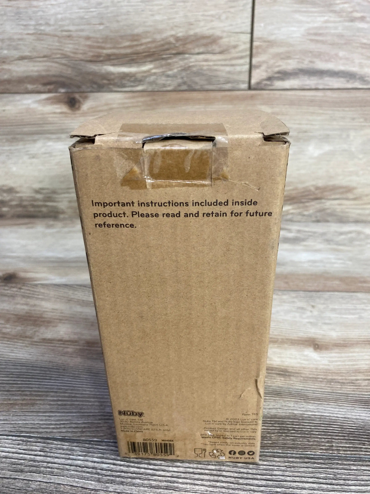 Rear of Nuby Thirsty Kids Flip-It Reflex stainless steel cup 10oz box showing printed instruction notice and barcode on wooden surface