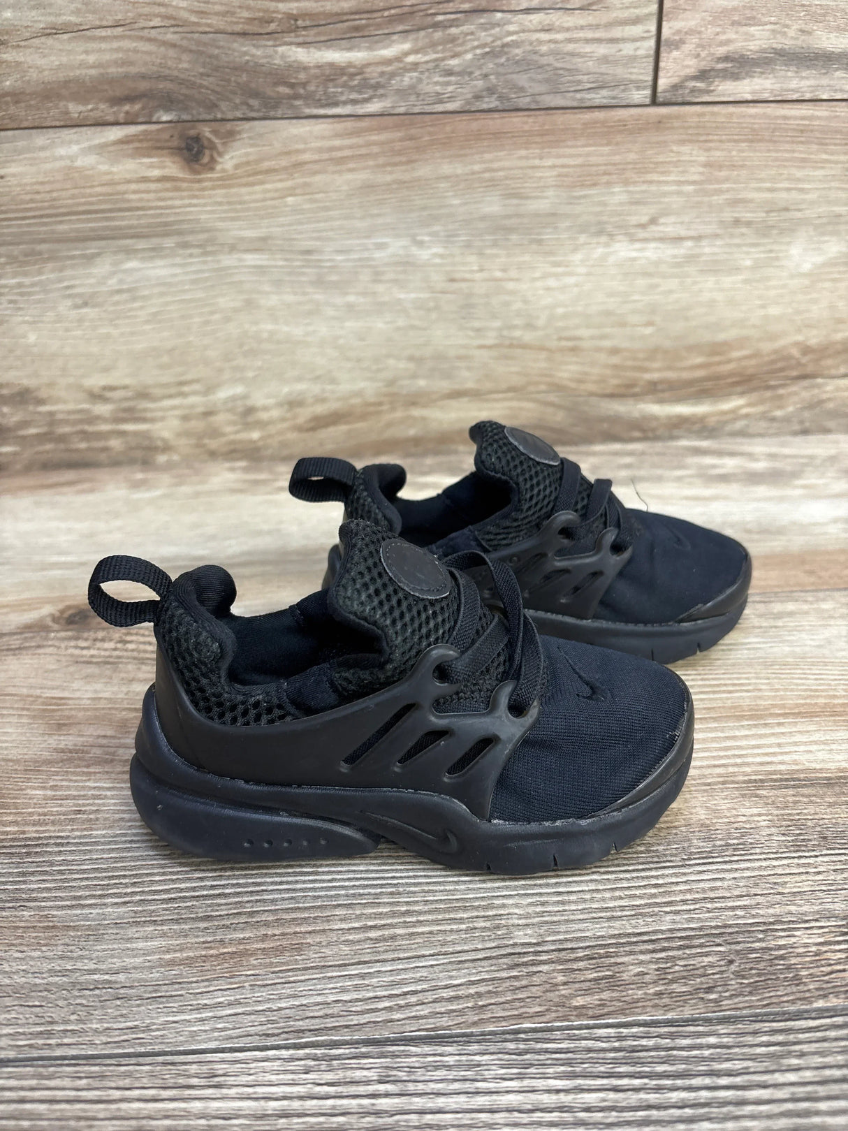 Black toddler Nike sneakers with mesh fabric and rubber soles on wooden floor