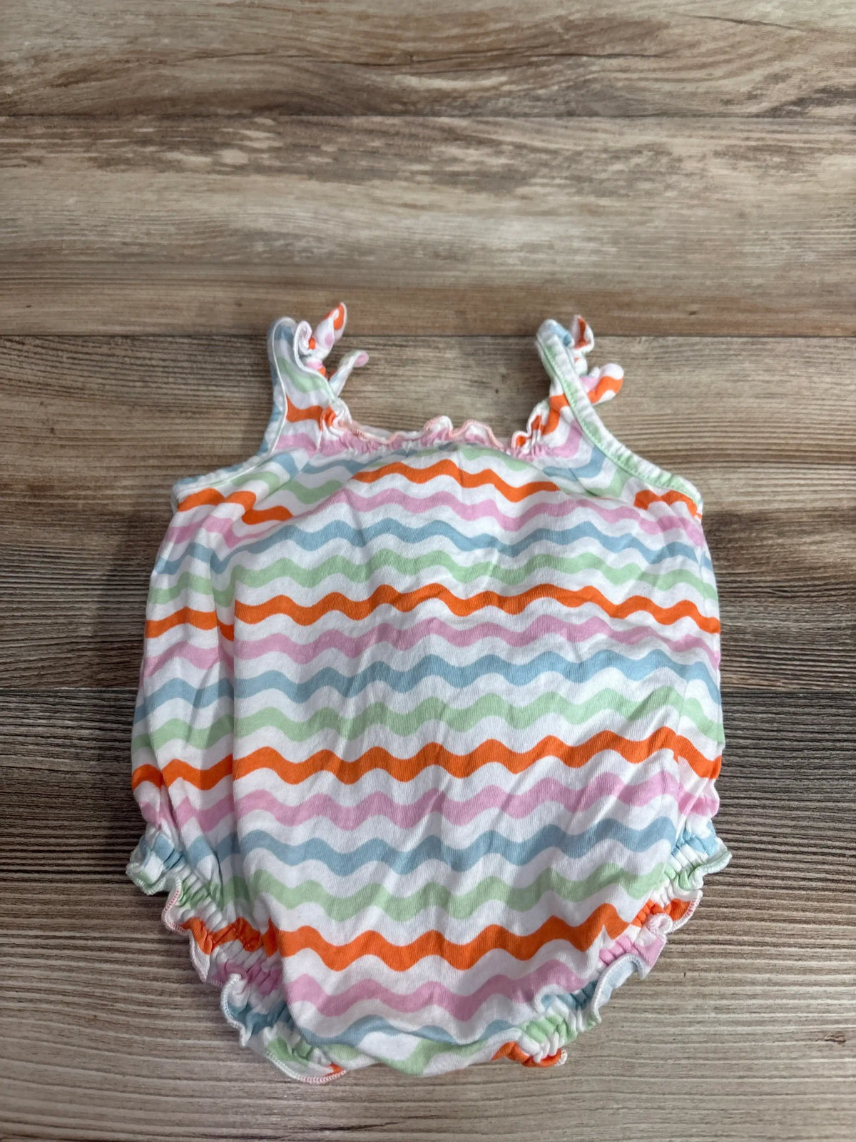 Flat lay of Old Navy bubble romper, white with multicolor wavy stripes, knotted straps and elastic leg openings on light wood