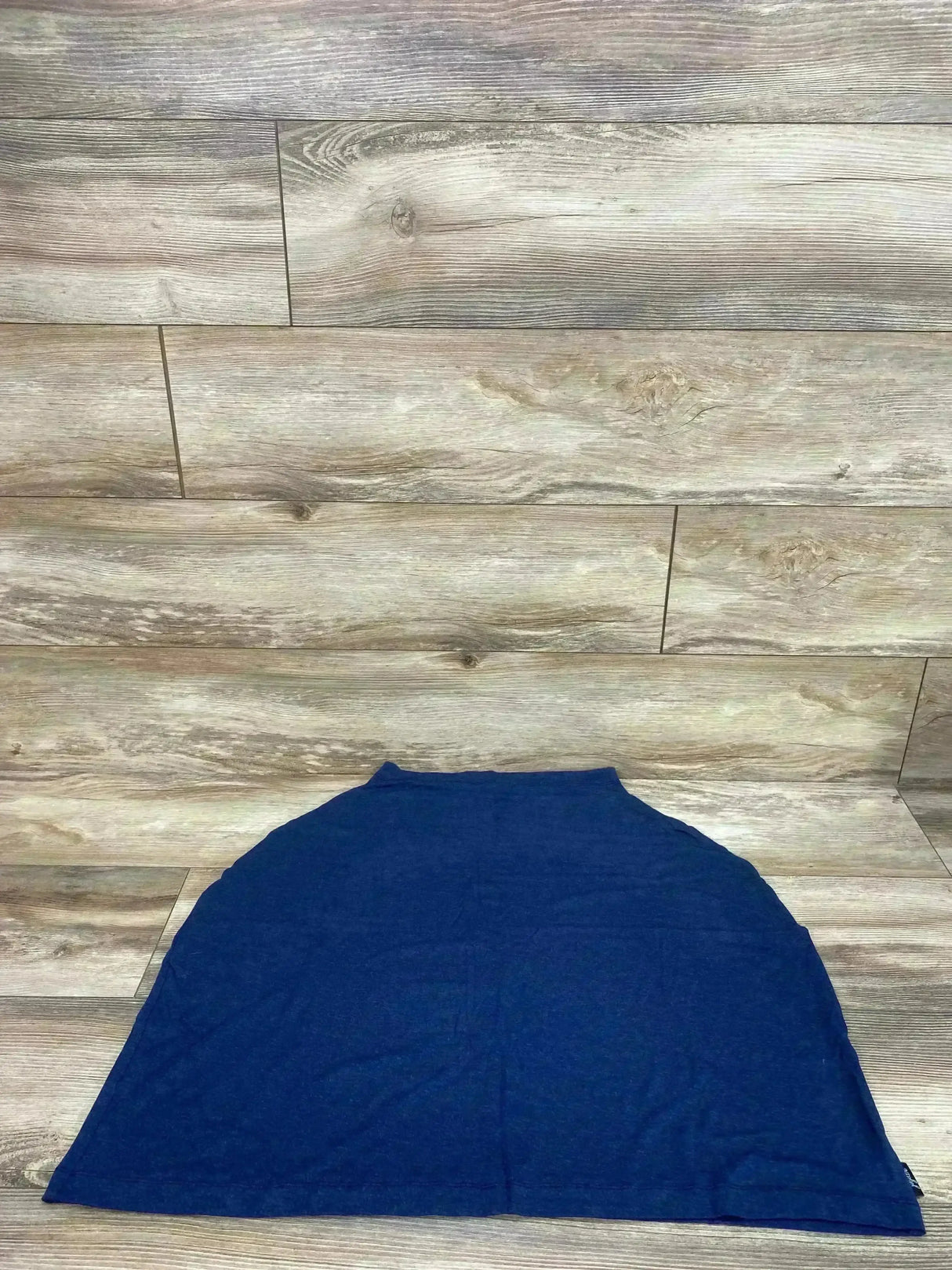 Flat lay of Jujube 6-in-1 navy car seat cover showing semi-circular shape and neck opening on wood plank floor