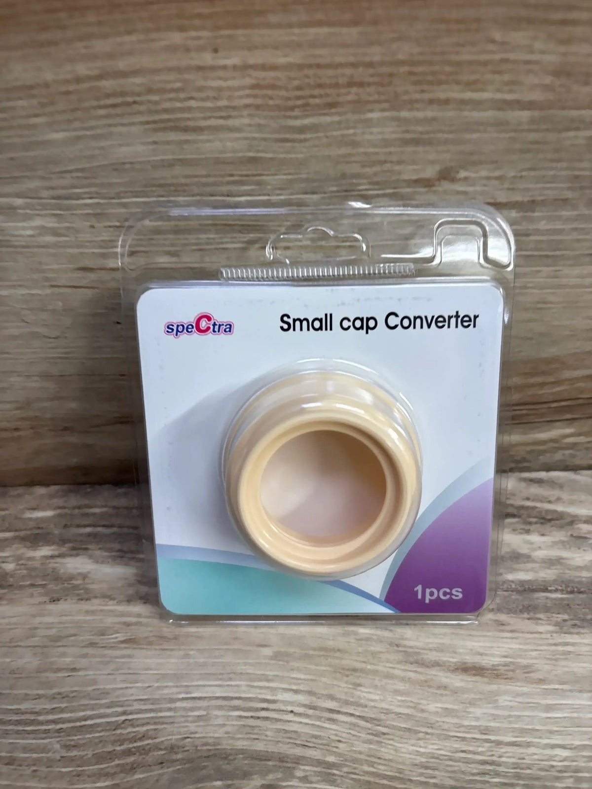 Front view of Spectra small cap converter in blister pack showing beige converter ring and visible packaging text 'Small cap Converter' on wooden background
