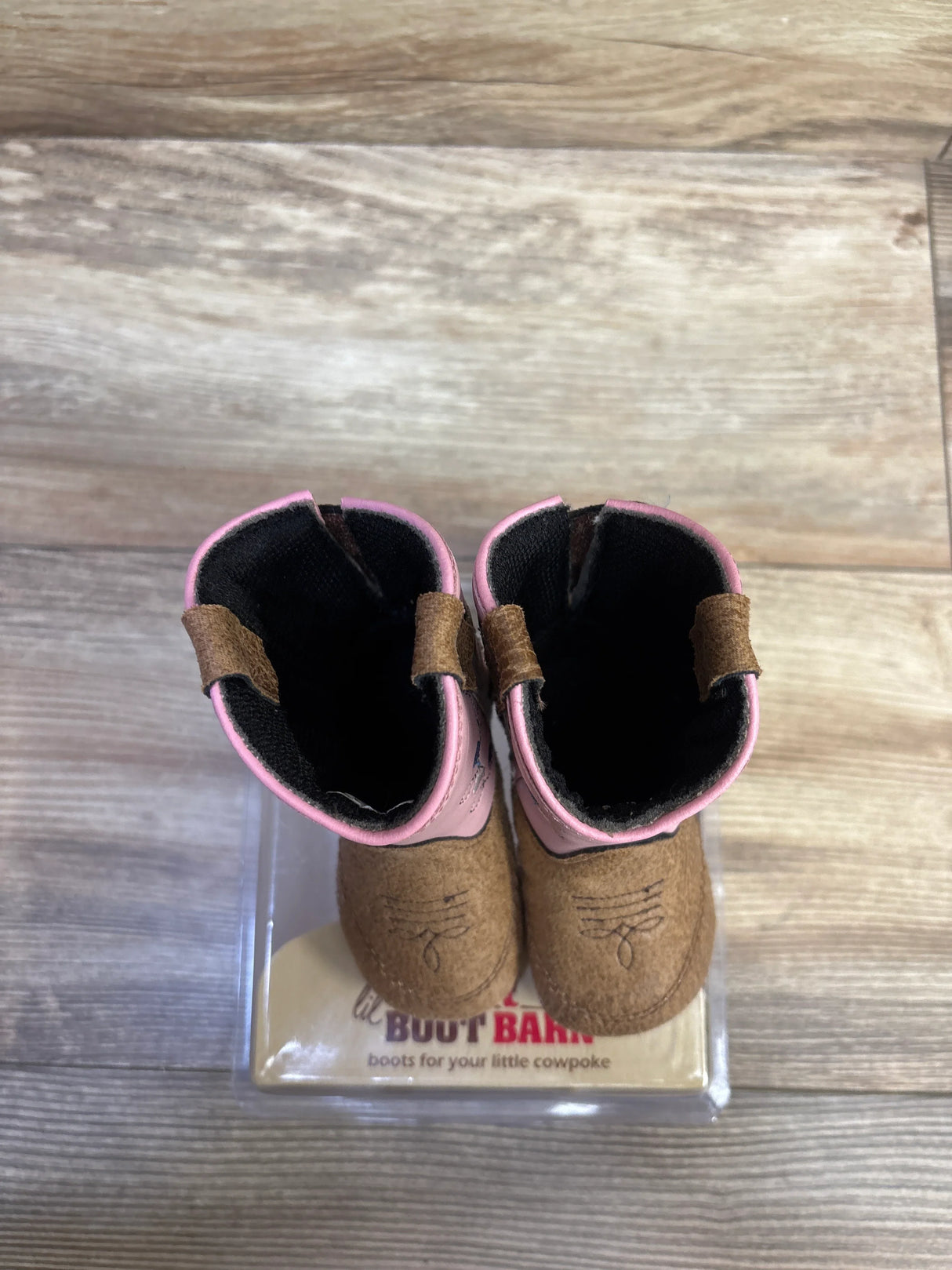 Top-down view of Poppets toddler cowboy boots showing brown suede toes, pink shafts with pull tabs on wood background