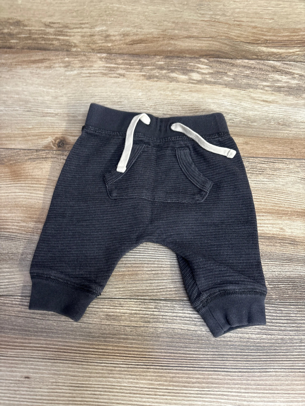 Black waffle knit baby pants with white drawstring and front pocket on wooden background