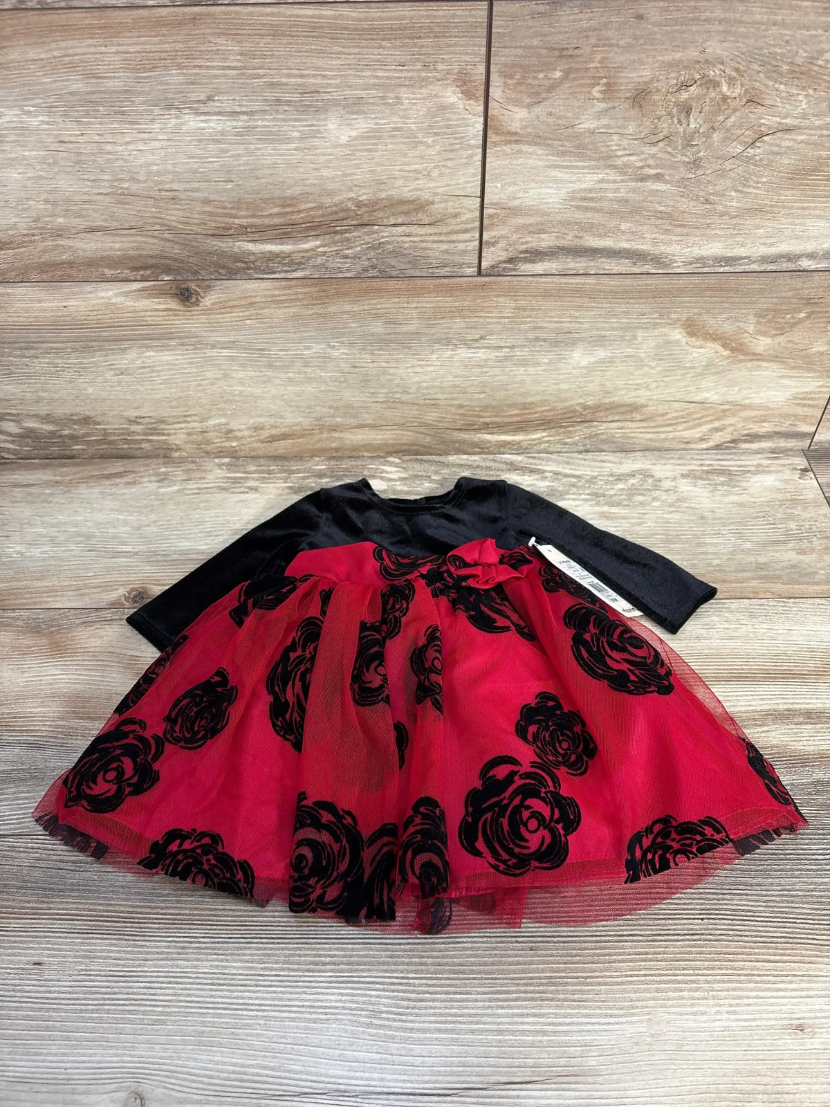 Flat lay of Mia & Mimi velvet long-sleeve baby dress showing red tulle skirt with black floral velvet burnout on wooden floor
