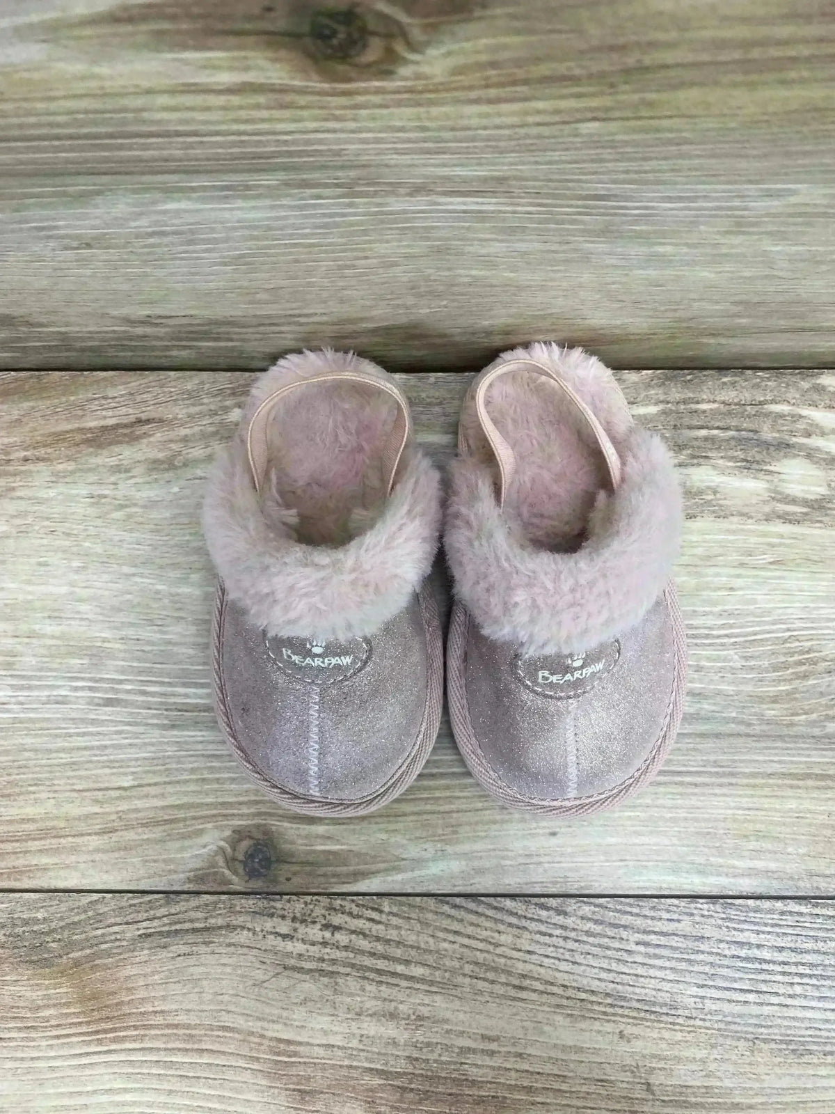 Overhead view of BEARPAW Rebecca suede slippers showcasing light pink sheepskin lining and faux-fur cuff on wood plank background