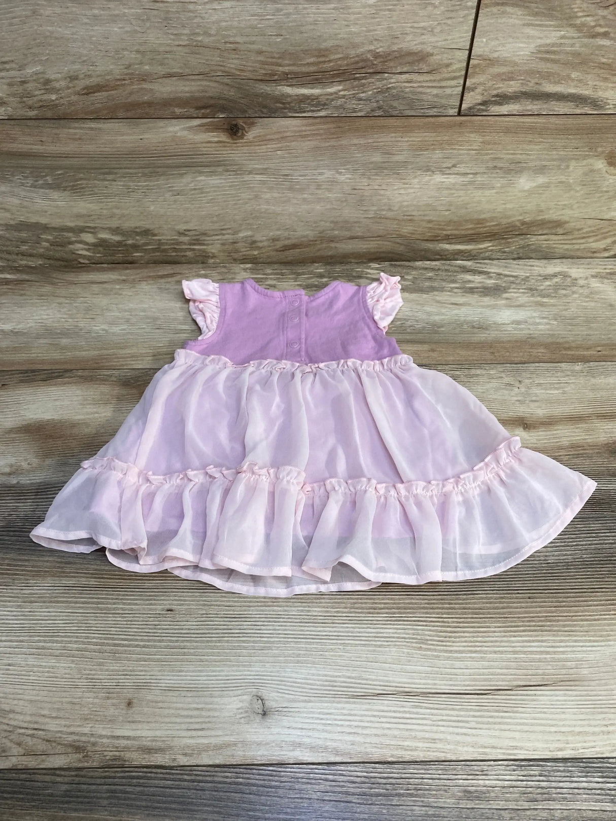 Flat lay of purple Peter Pan and Wendy baby dress with bloomers, ruffled chiffon skirt and snap-back bodice on wood floor