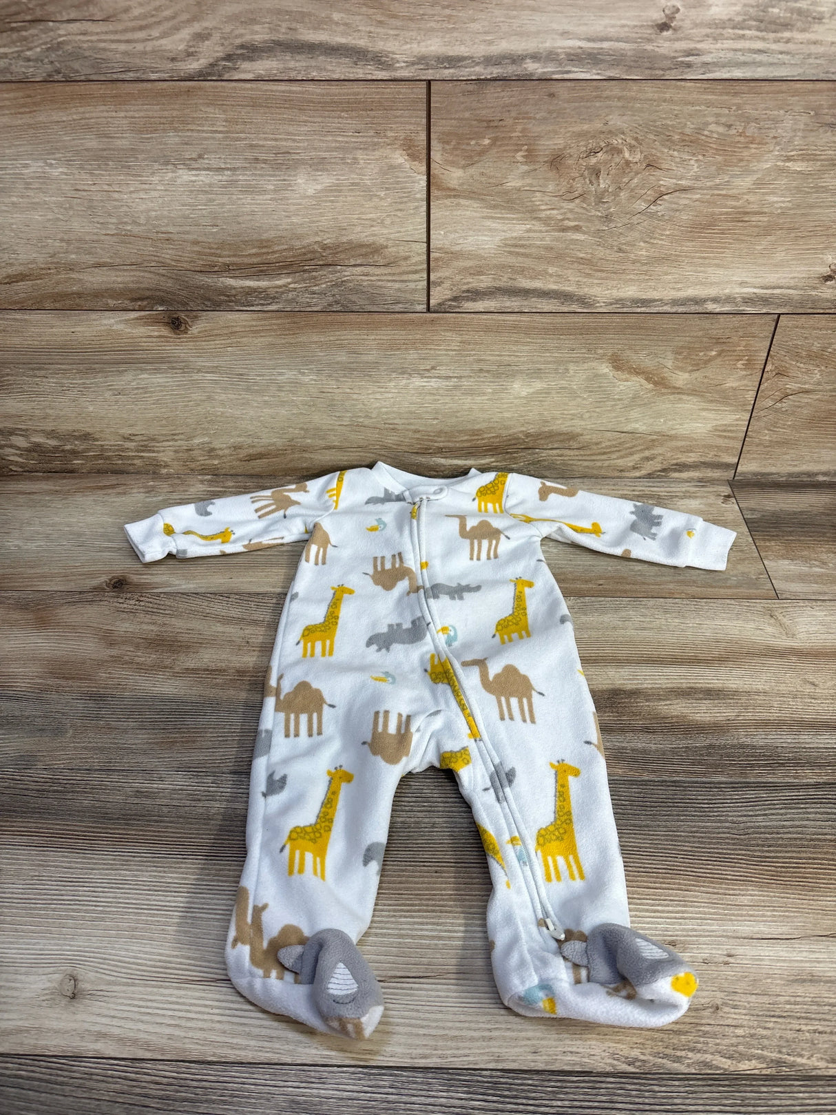 Flat-lay of white Simple Joys footed blanket sleeper (size 3-6M) showing yellow giraffe and camel print, front zipper, on wood floor