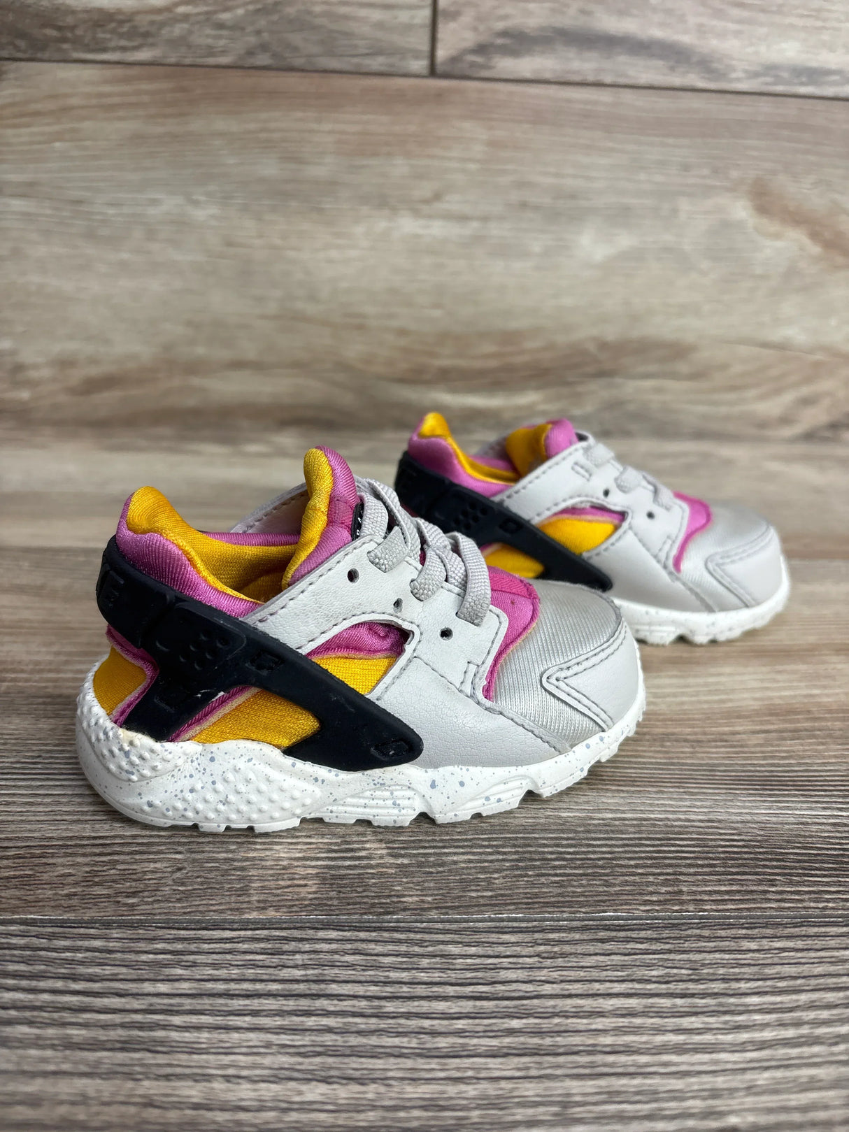 Toddler sneakers with gray, pink, yellow, and black accents on wood background