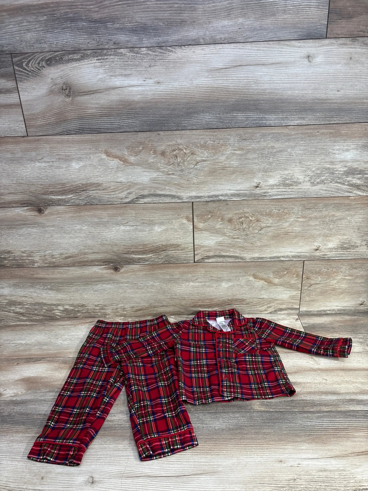 Red plaid kids pajama set with long sleeves and pants, laid on wood floor