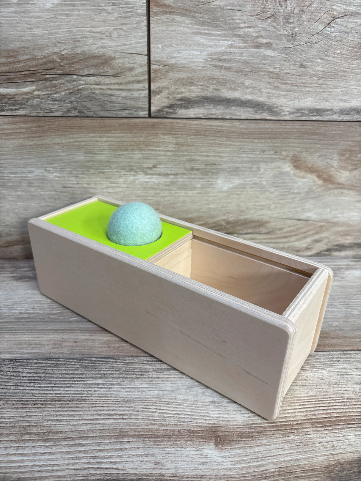 Wooden storage box with green felt ball on a green platform against wood background