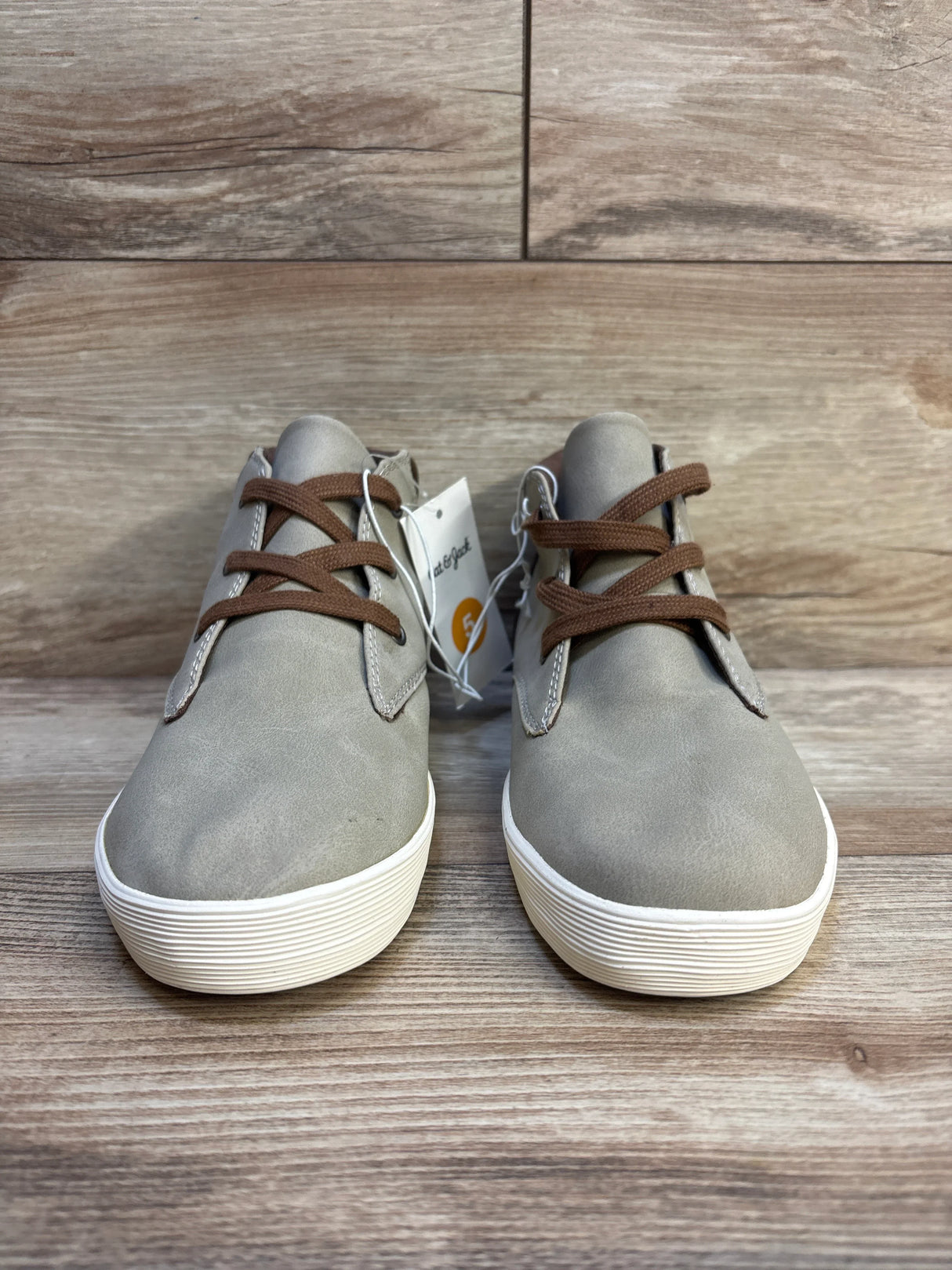 Gray kids' sneakers with brown laces on wood floor, gently used children's shoes