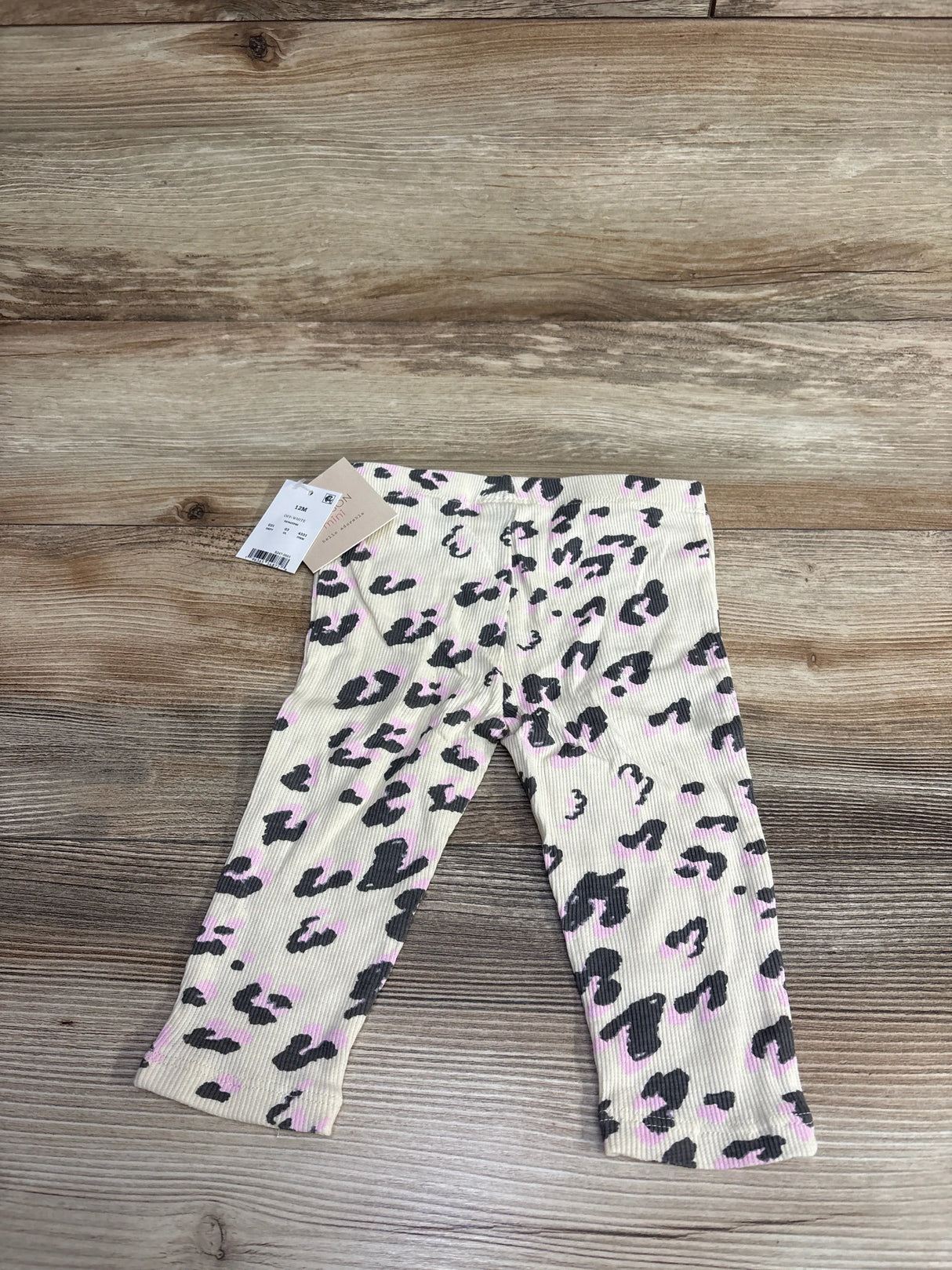 Baby leggings in cream with black and pink leopard print laid flat on wood surface, size 12M with tags