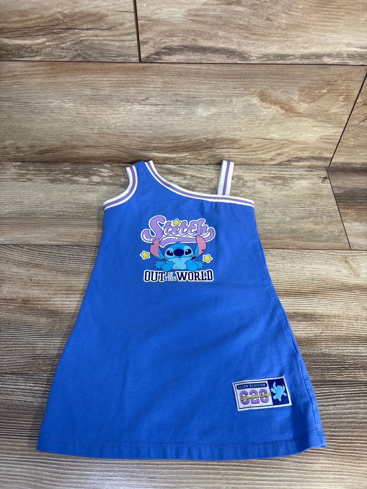Front view of Disney Stitch tank dress in blue, size 2T, showcasing its sleeveless style and Stitch graphic on a wood floor