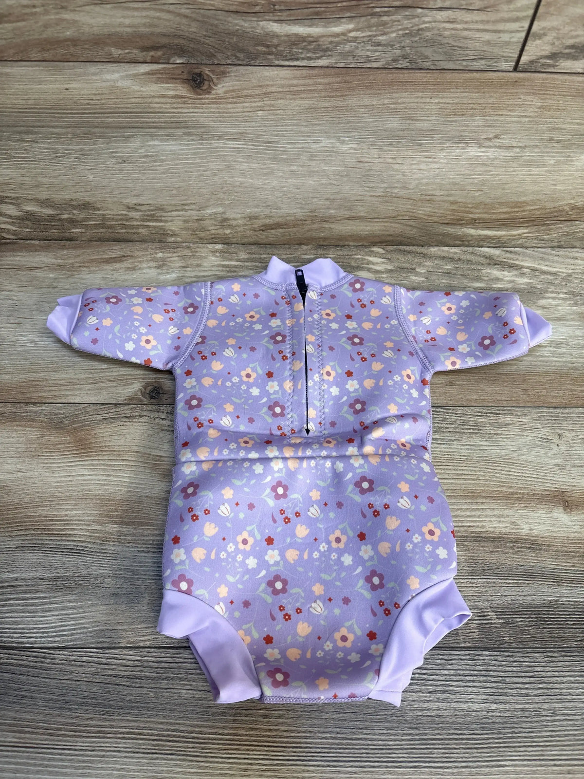 Front view of Splash About Happy Nappy Wetsuit Lilac Spring showcasing floral print and front zipper on a wood background