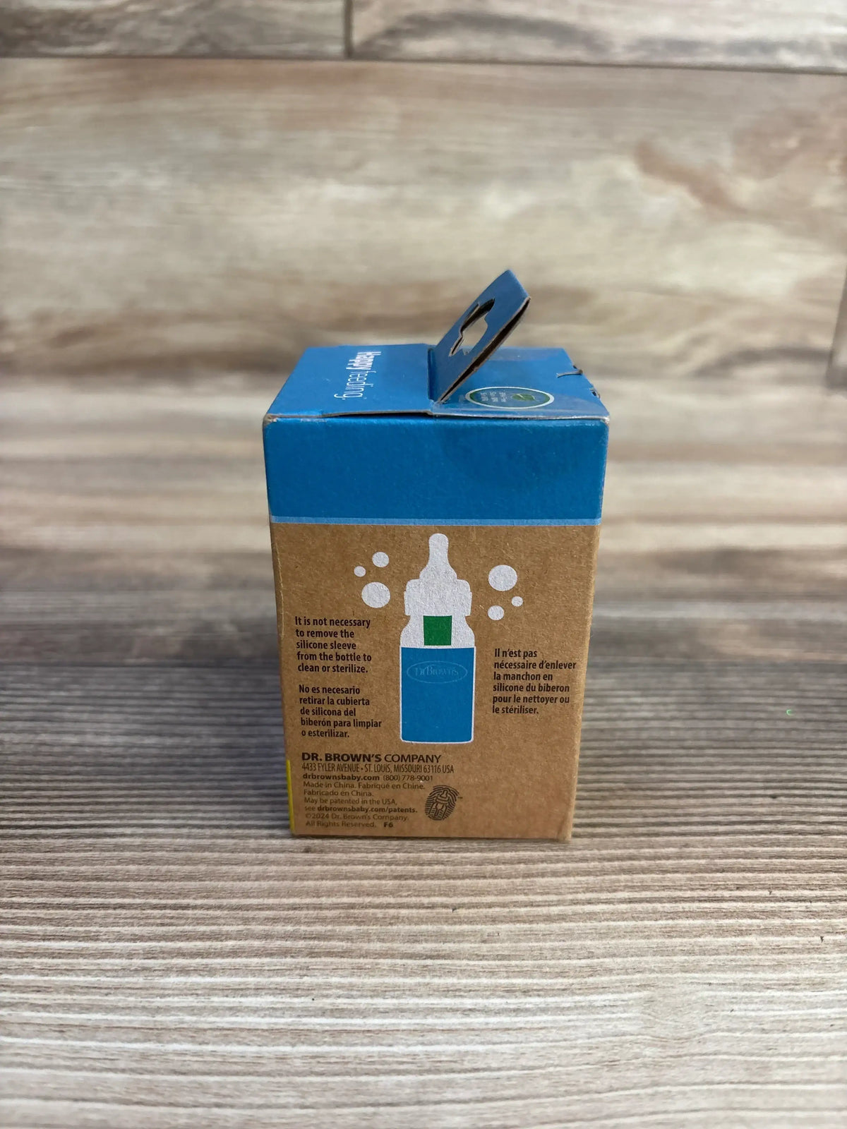 Front view of Dr. Brown's narrow silicone bottle sleeve box with blue top and hang tab on wood table