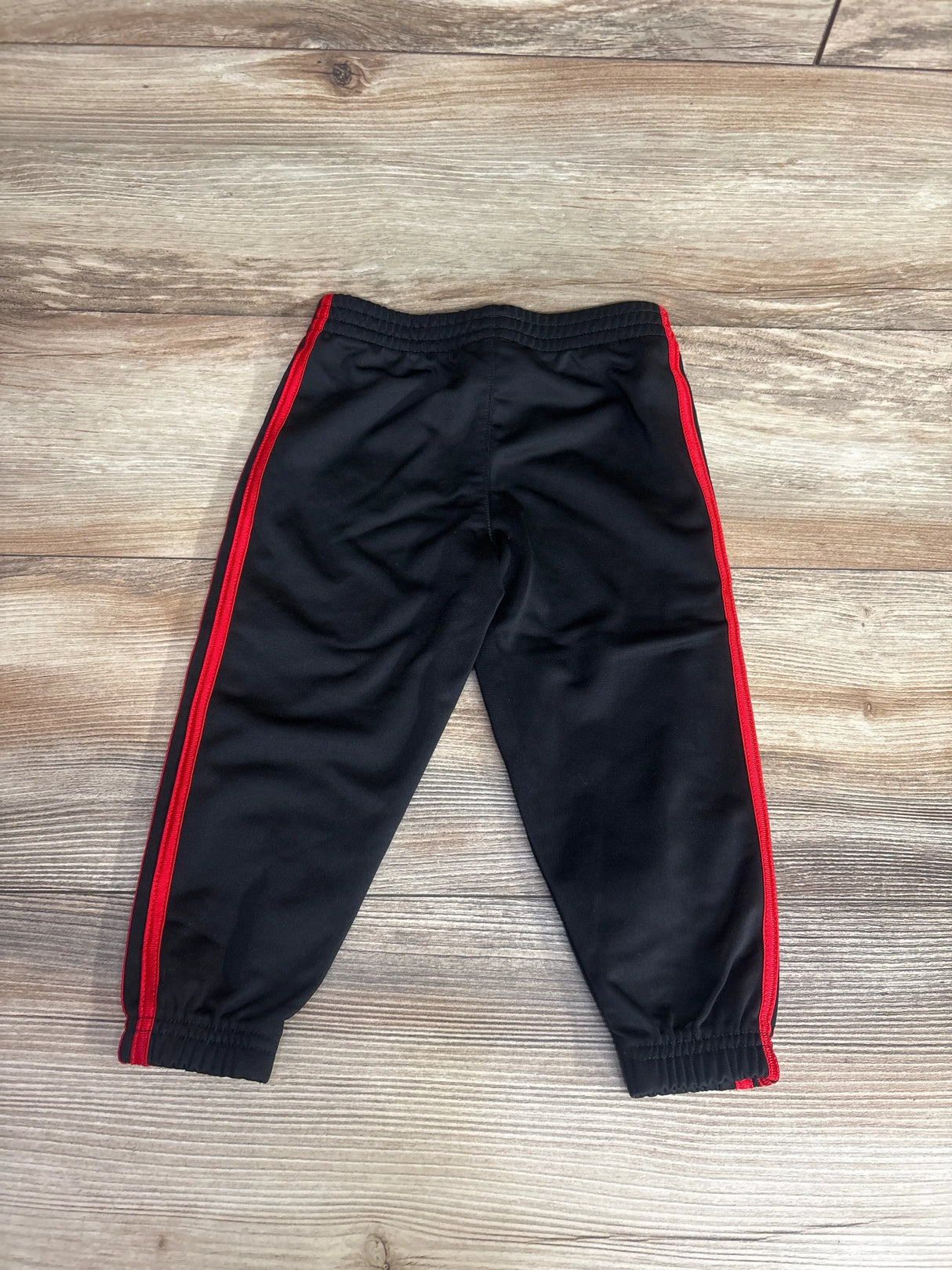 Black kids track pants with red side stripes on wooden floor