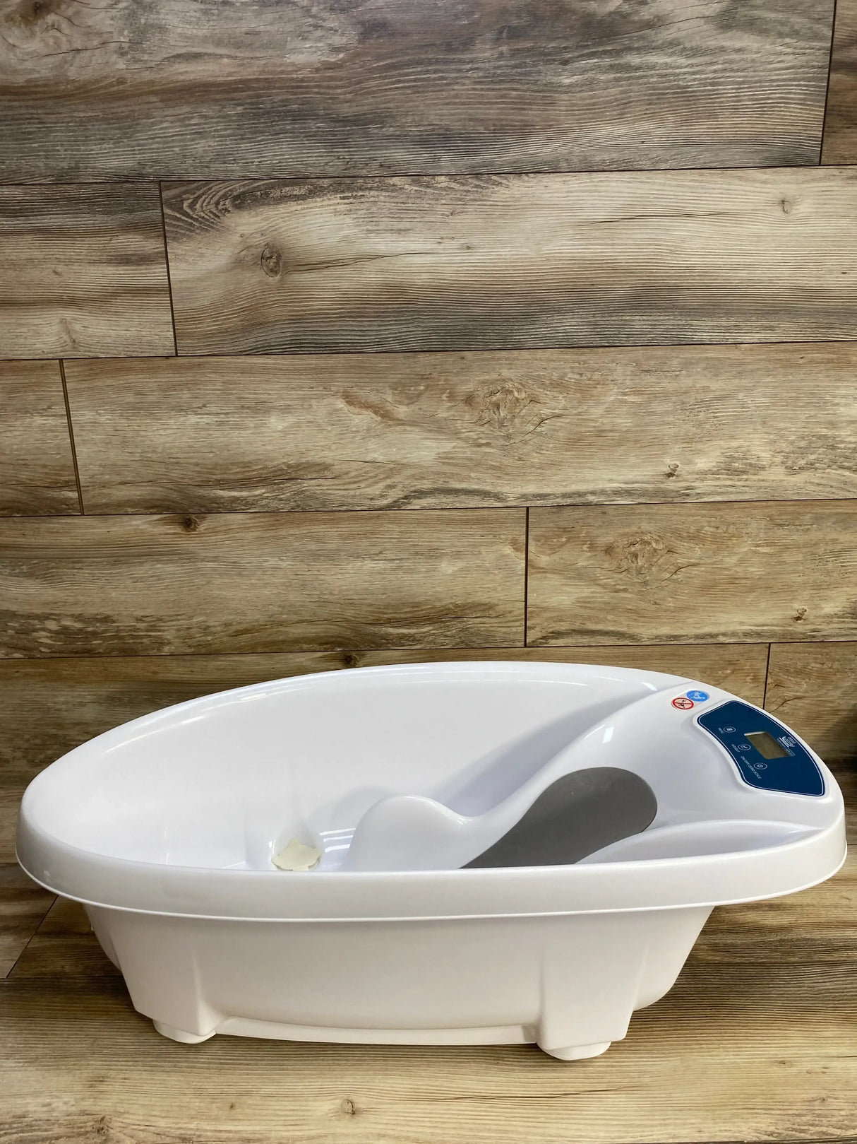 Front view of AquaScale 3-in-1 infant tub showcasing built-in digital scale and contoured baby support with wood plank background