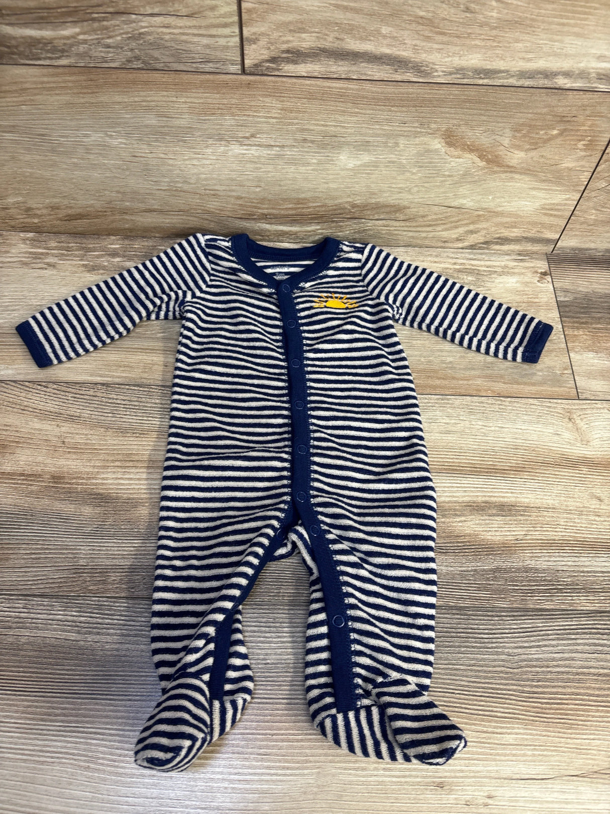 Striped navy and white footed baby sleeper with yellow whale embroidery on wood floor